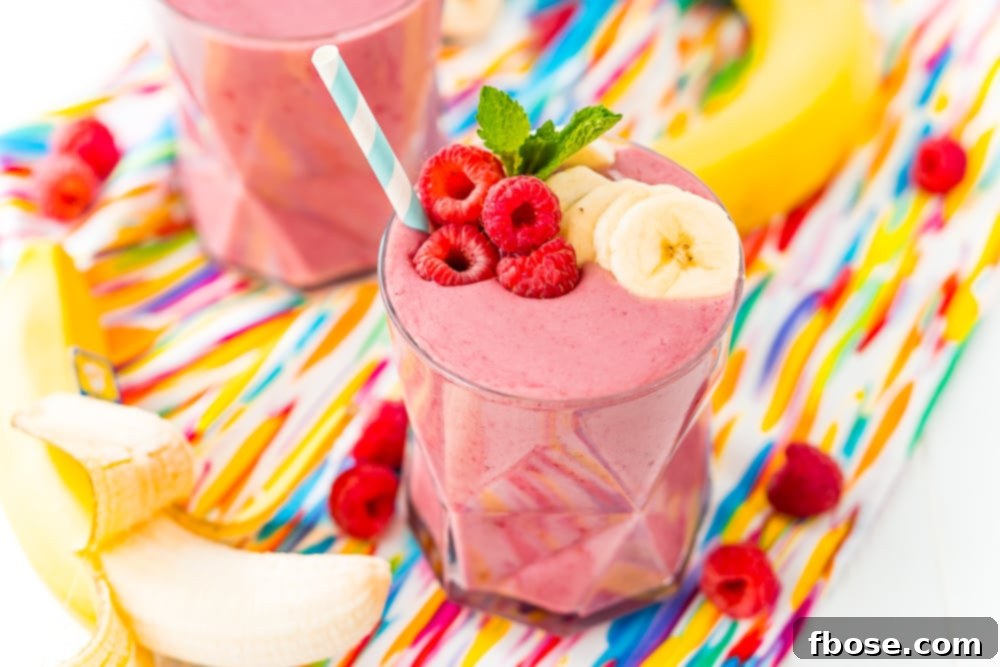 Berry Banana Bliss 7 Wide photo of a glass filled with a raspberry banana smoothie with bananas and raspberries on the side.