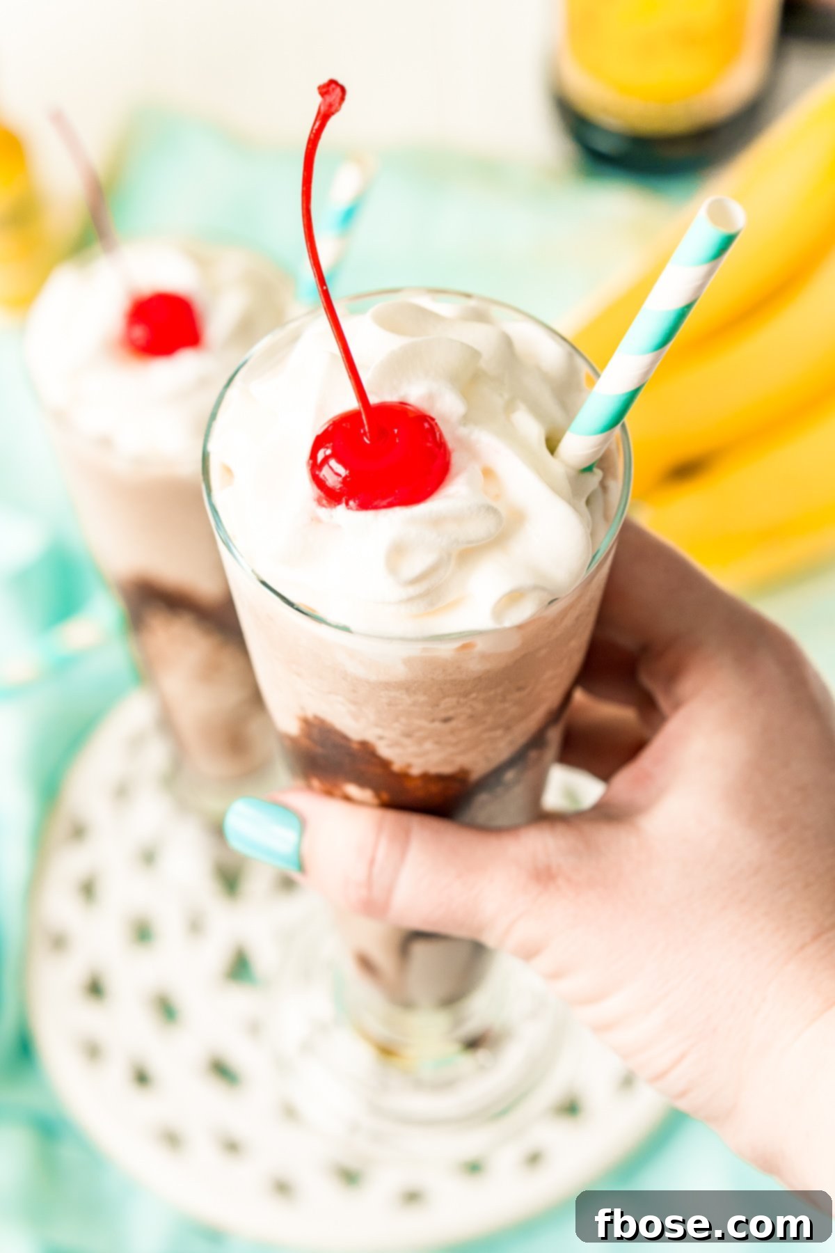 Woman's hand holding a frozen cocktail with whipped cream and a cherry on top.