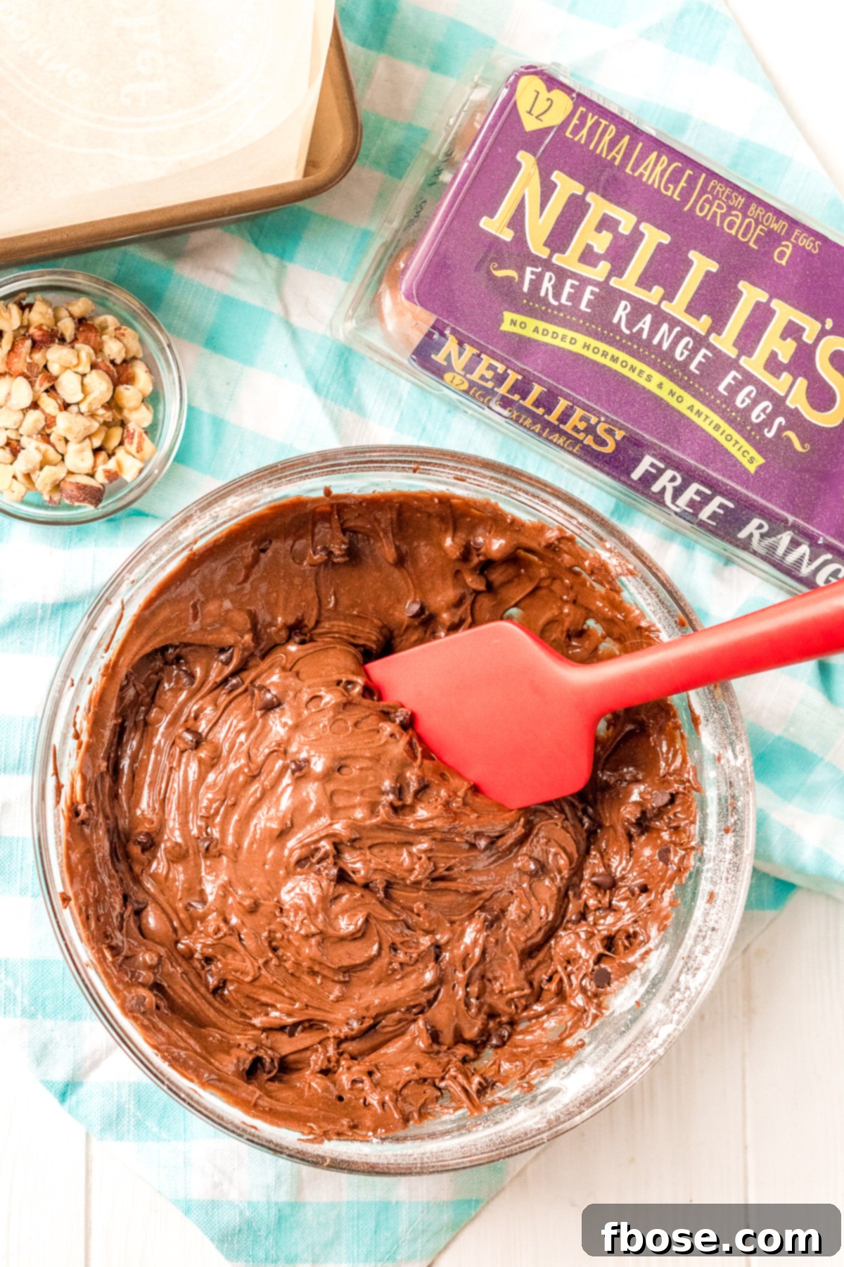 Brownie batter in a large mixing bowl with a smaller bowl of chopped hazelnuts next to it.