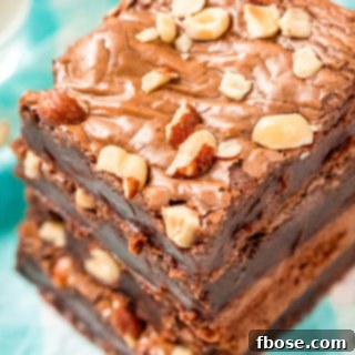 Overhead angled photo of a stack of hazelnut brownies with hazelnuts on top on a blue and white napkin.