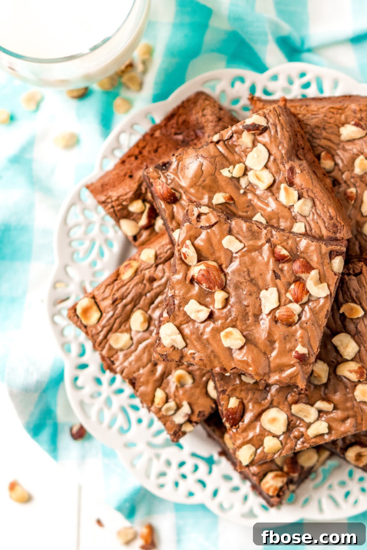 Brownies with chopped hazelnuts on a white plate with a blue and white napkin.