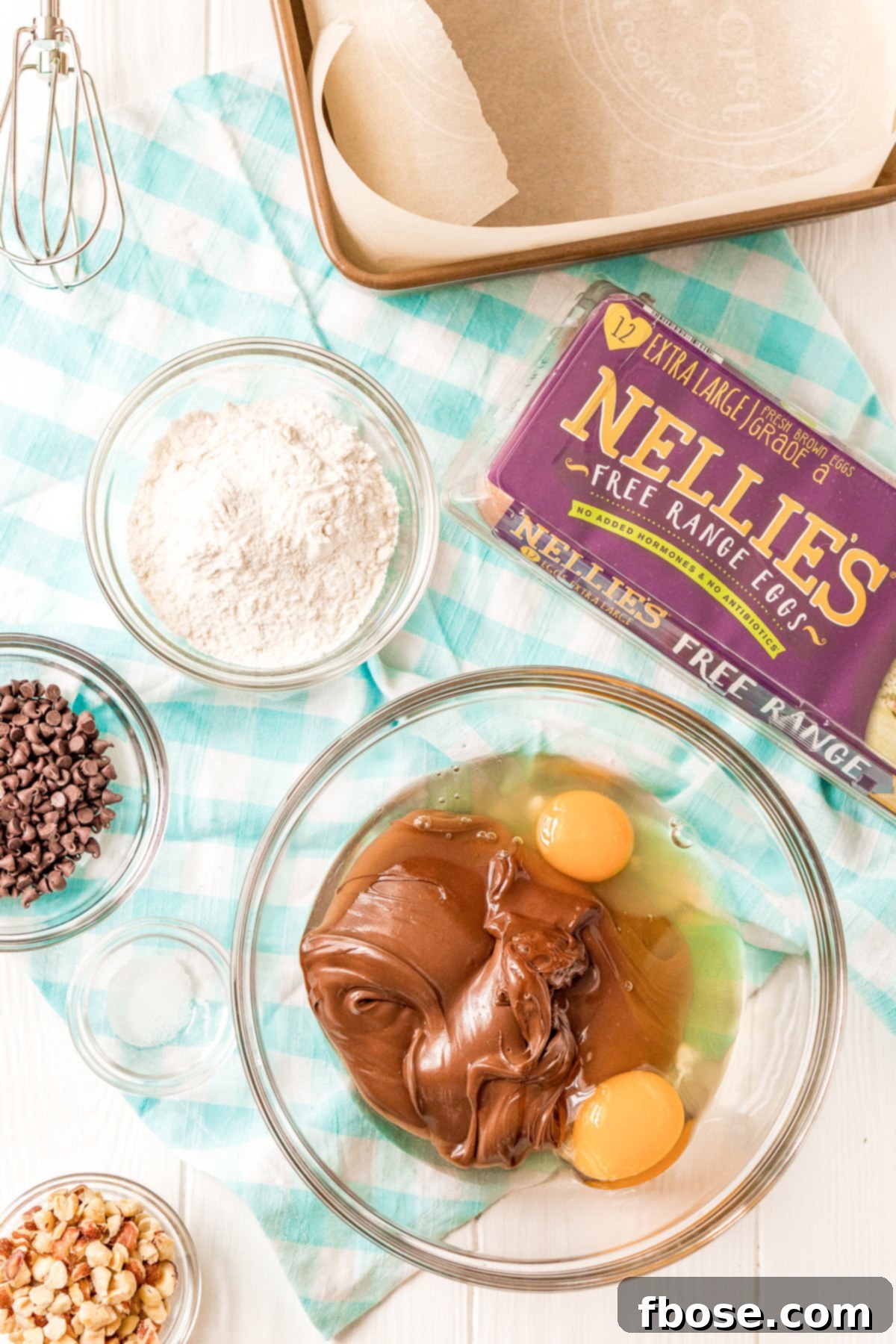 Hazelnut spread in a large bowl with two cracked eggs. Other ingredients in prep bowls scattered around.