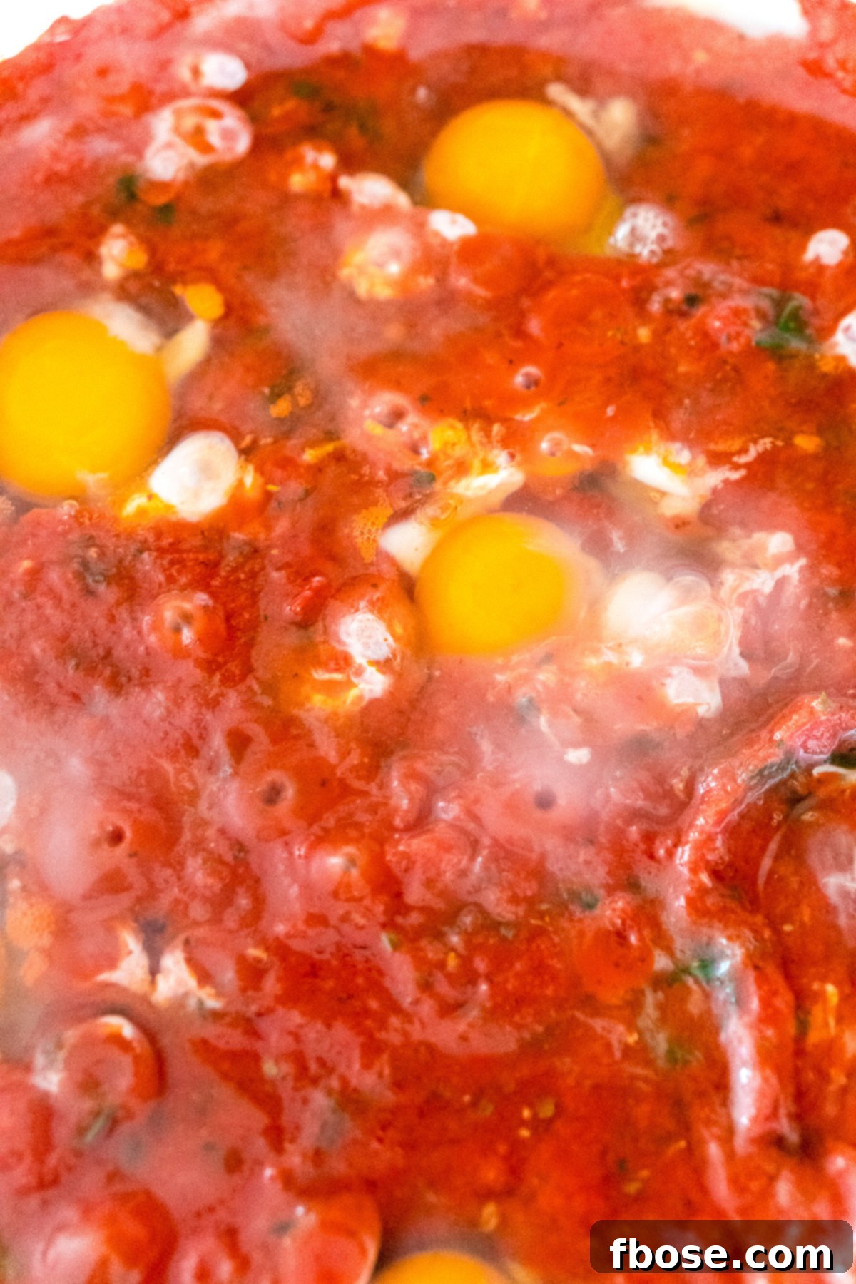 Close up photo of eggs being poached in tomato sauce. A captivating close-up of eggs gently poaching in the vibrant tomato sauce, showcasing the transformation as they cook to perfection.