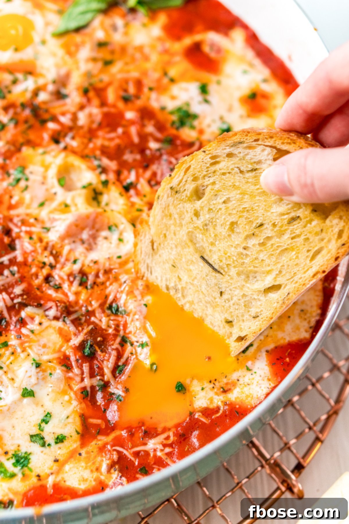 Crusty bread being dipped into a poached egg in a batch of Eggs In Purgatory. Crusty bread being dipped into a runny poached egg yolk, showcasing the ultimate comfort food experience of Eggs in Purgatory.