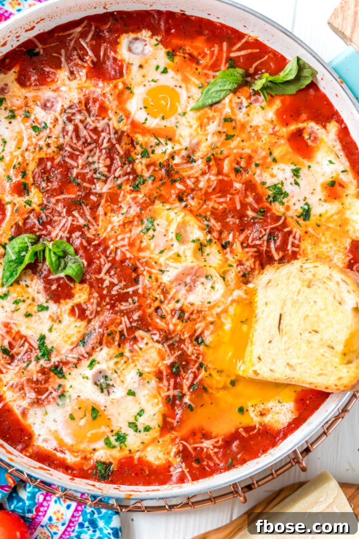 Overhead photo of a slice of bread being dipped in a runny egg yolk in a poached egg dish. A close-up, tempting shot of crusty bread being dipped into a luscious, runny egg yolk from a poached egg in the tomato sauce.
