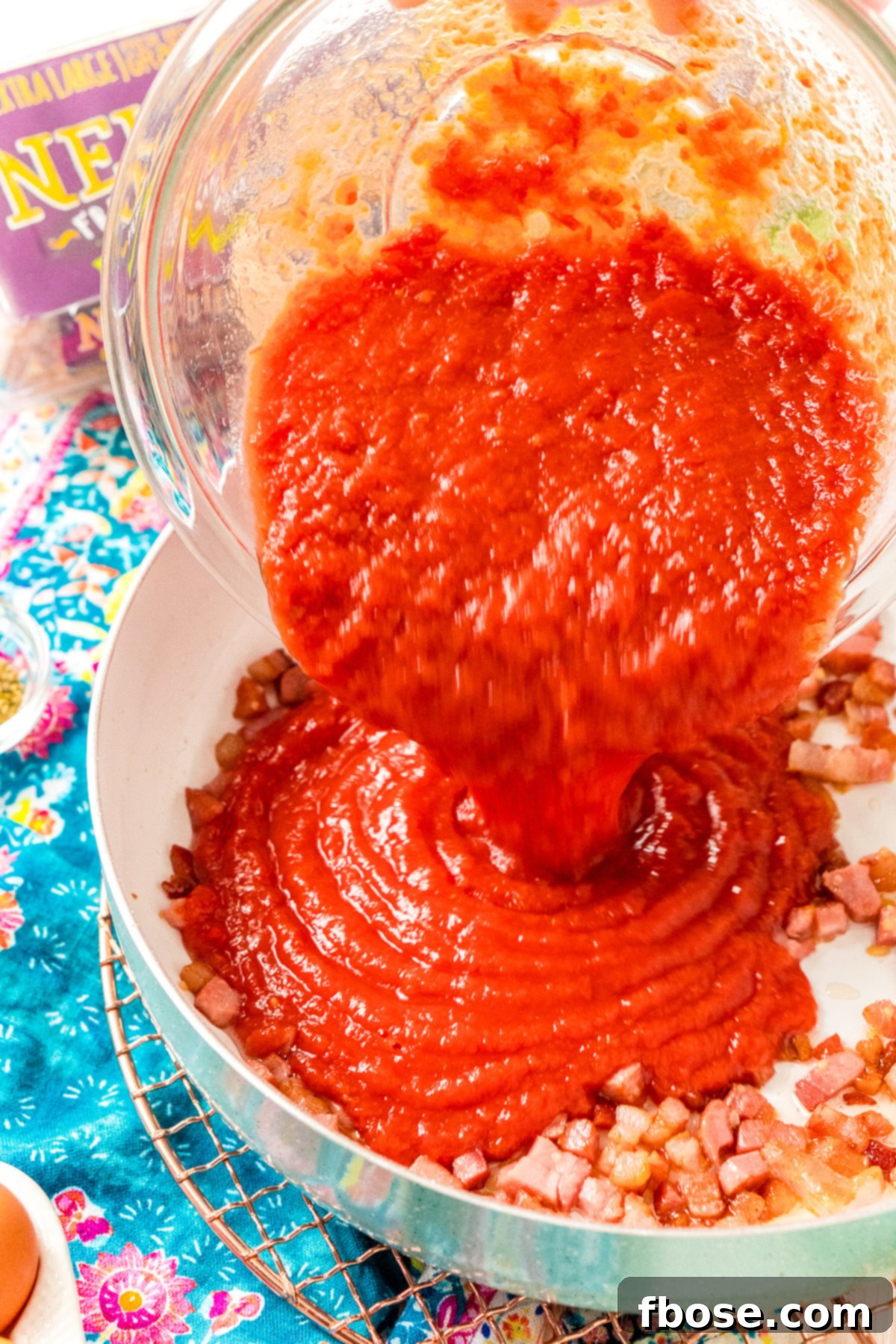 Crushed Tomatoes being added to a skillet with pancetta and garlic. Adding the star ingredient: crushed tomatoes being poured into the skillet with the cooked pancetta and garlic, setting the stage for the flavorful sauce.