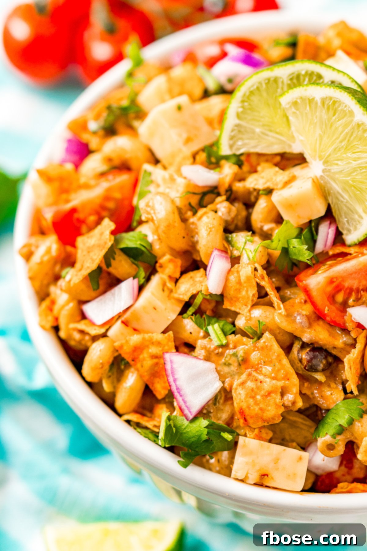 A large white bowl filled with vibrant Taco Pasta Salad, featuring spiral pasta, ground beef, colorful vegetables, and crushed Doritos, ready for serving at a summer gathering.