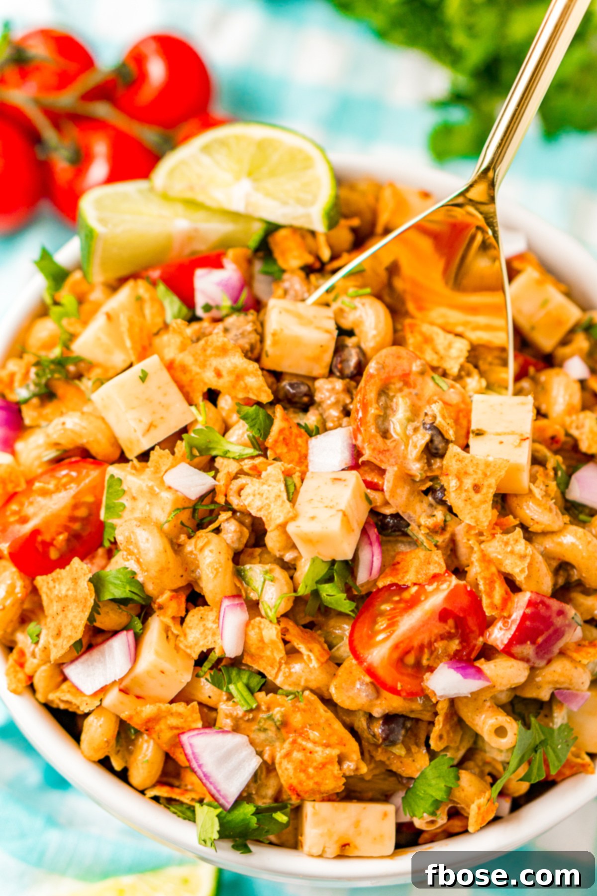 A gold serving spoon scooping a generous portion of Taco Pasta Salad from a large white bowl, highlighting the dish's enticing texture and ingredients.