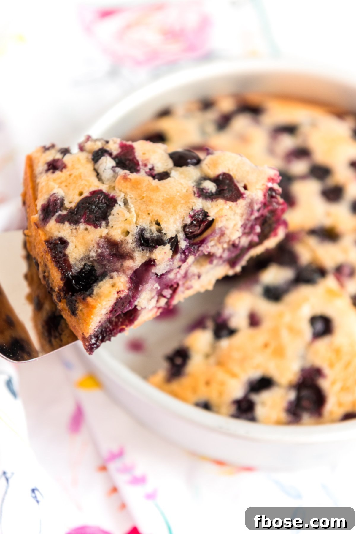 Piece of blueberry cake on a server being lifted out of the cake pan.