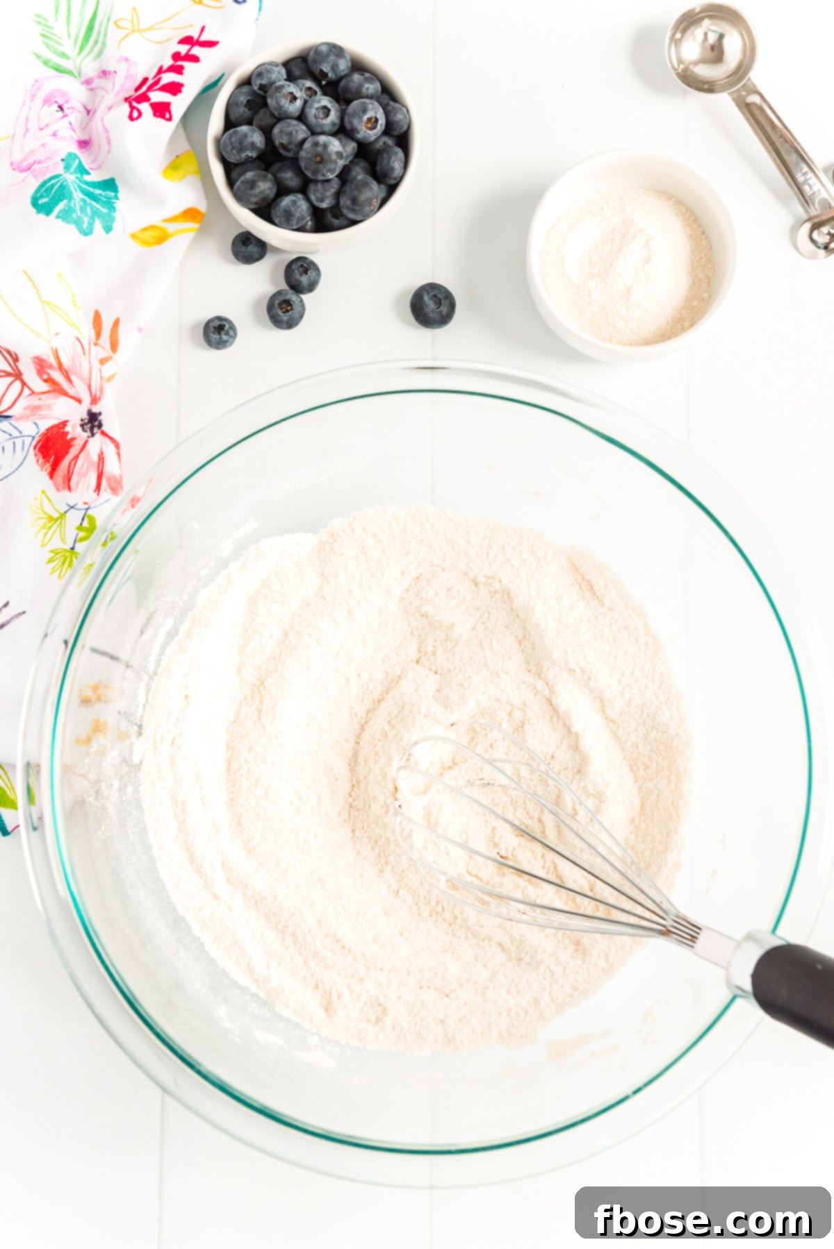 Flour, salt, and sugar being whisked together in a large glass bowl.