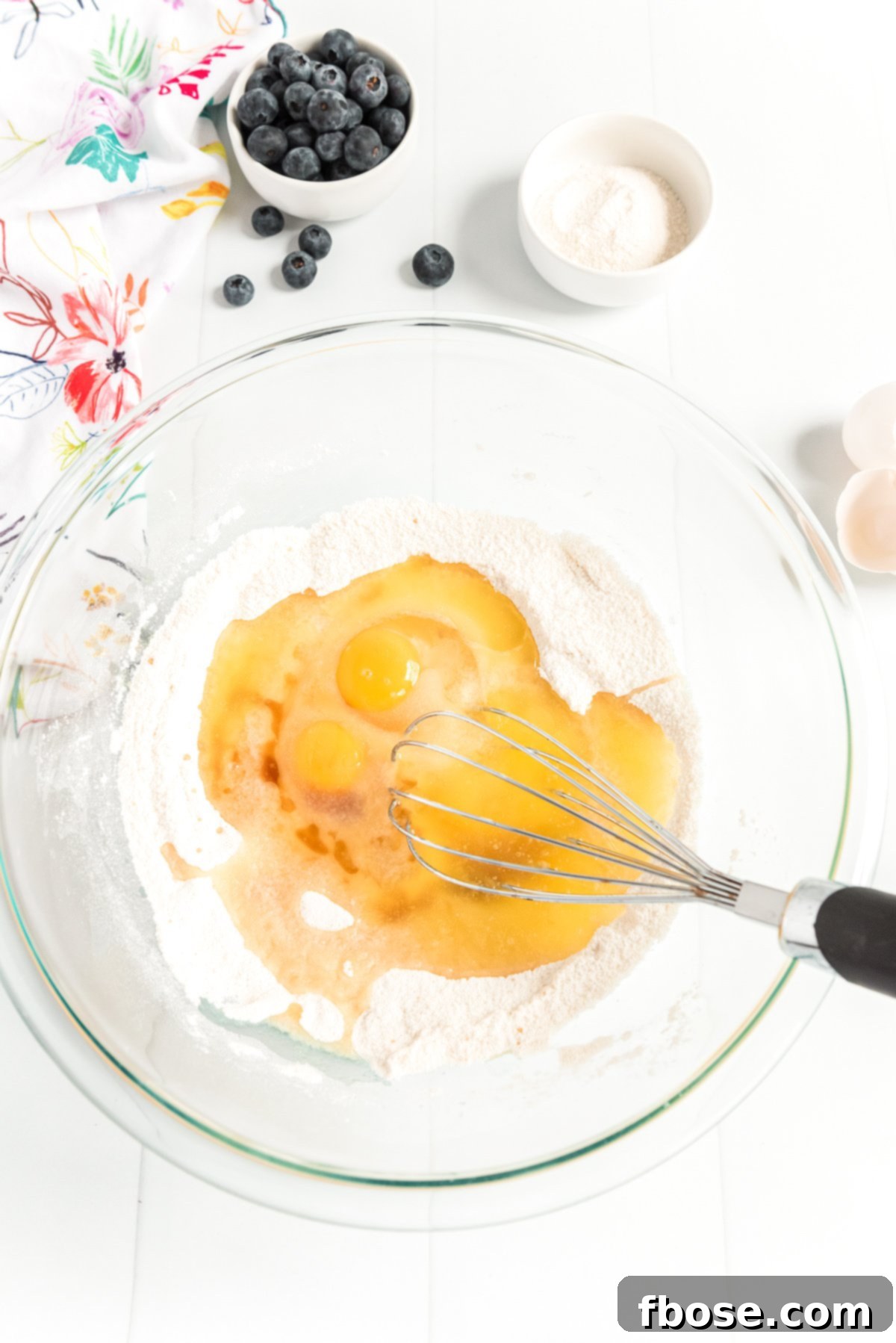 Eggs being mixed into flour and sugar in a large glass bowl.