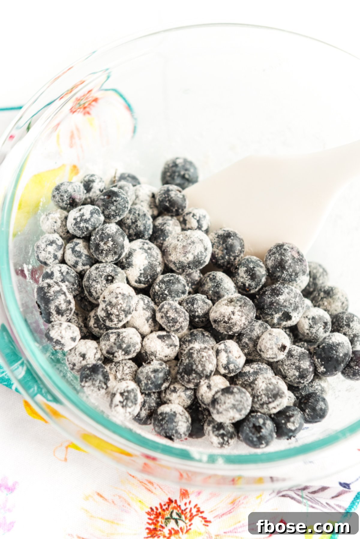 Blueberries being tossed with flour in a large glass bowl.
