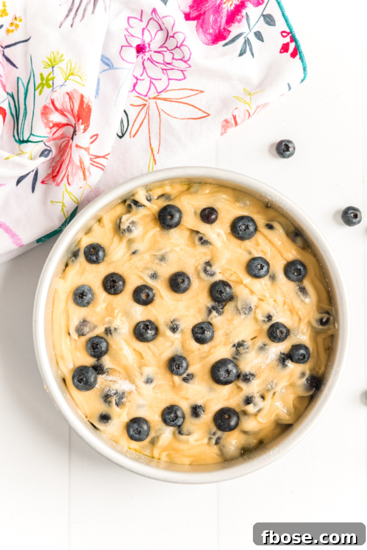 Blueberry cake batter in a round cake pan with a colorful floral napkin next to it.