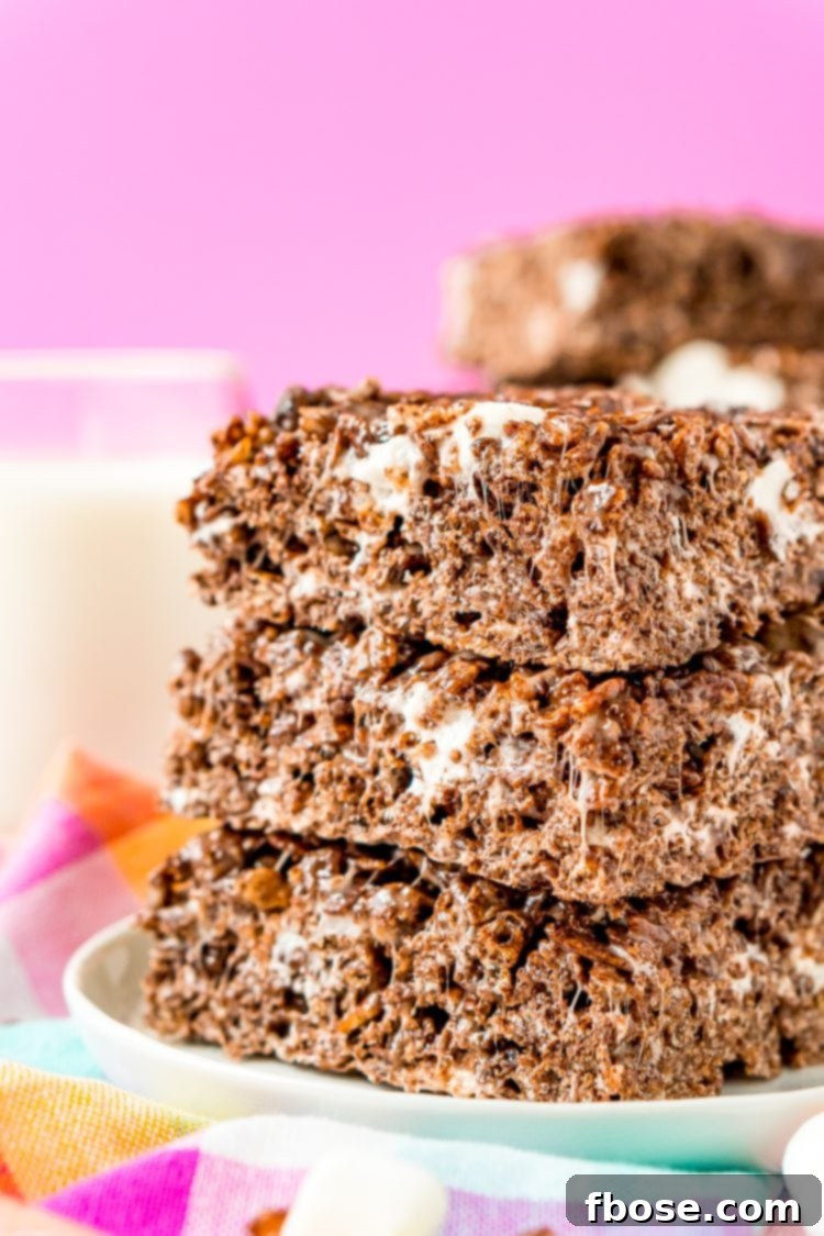 Cocoa Pebbles Crunch Bars 2 Stack of three cocoa pebbles no bake treats on a white plate on a colorful napkin with a glass of milk in the background.