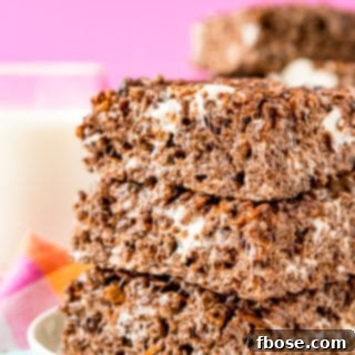 Stack of three cocoa pebbles no bake treats on a white plate on a colorful napkin with a glass of milk in the background.