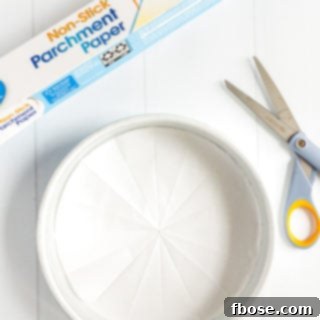 Parchment paper lined cake pan with a roll of parchment paper and pair of scissors next to it.