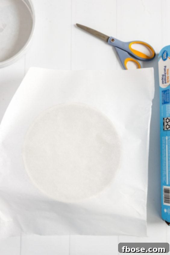 Parchment paper resting on a cake pan with the roll and a pair of scissors to the side.