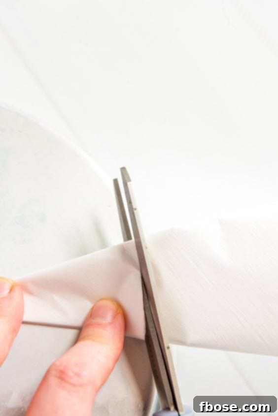 Folded parchment paper being cut to line a cake pan.