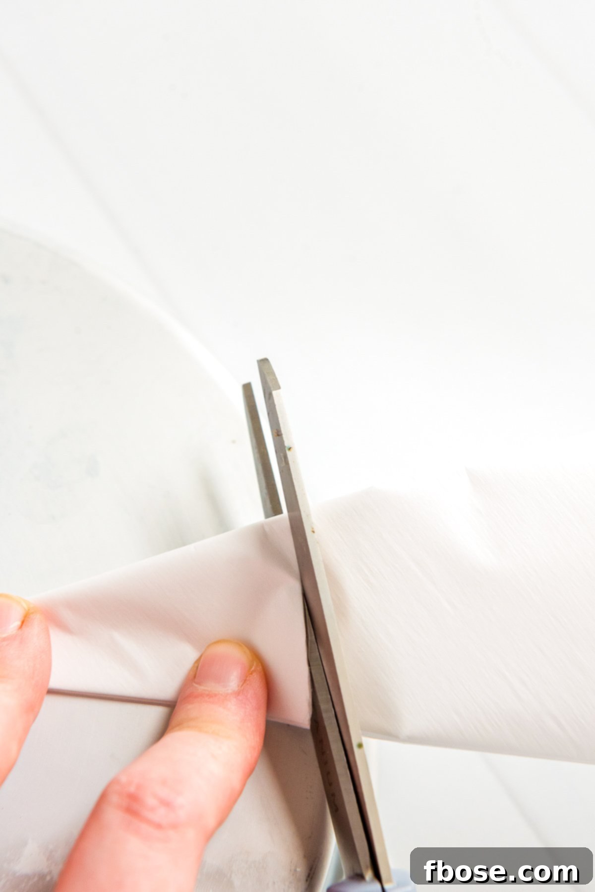 Folded parchment paper being carefully cut to match the curve of a cake pan.