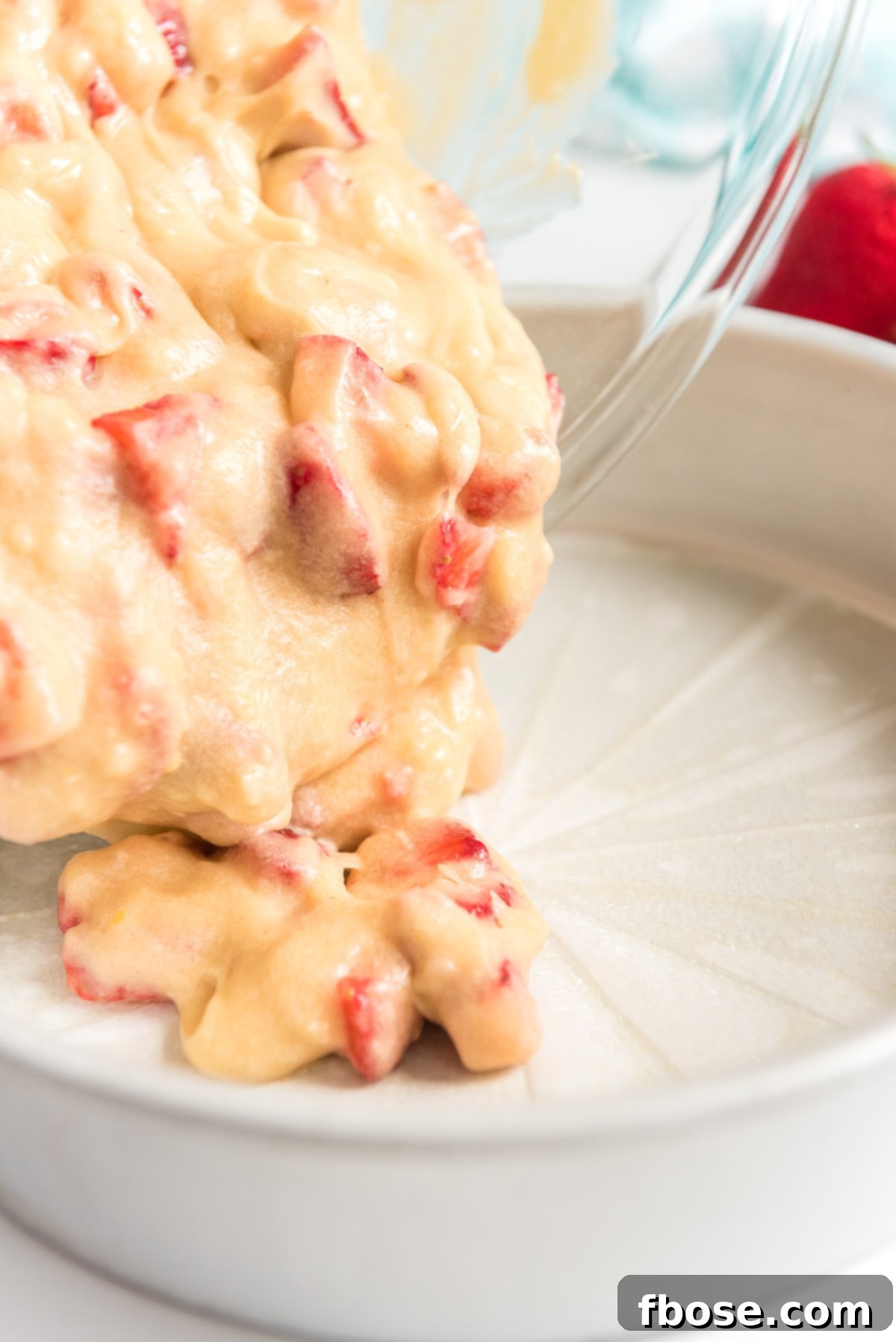Strawberry cake batter being carefully poured into a prepared cake pan lined with parchment paper.