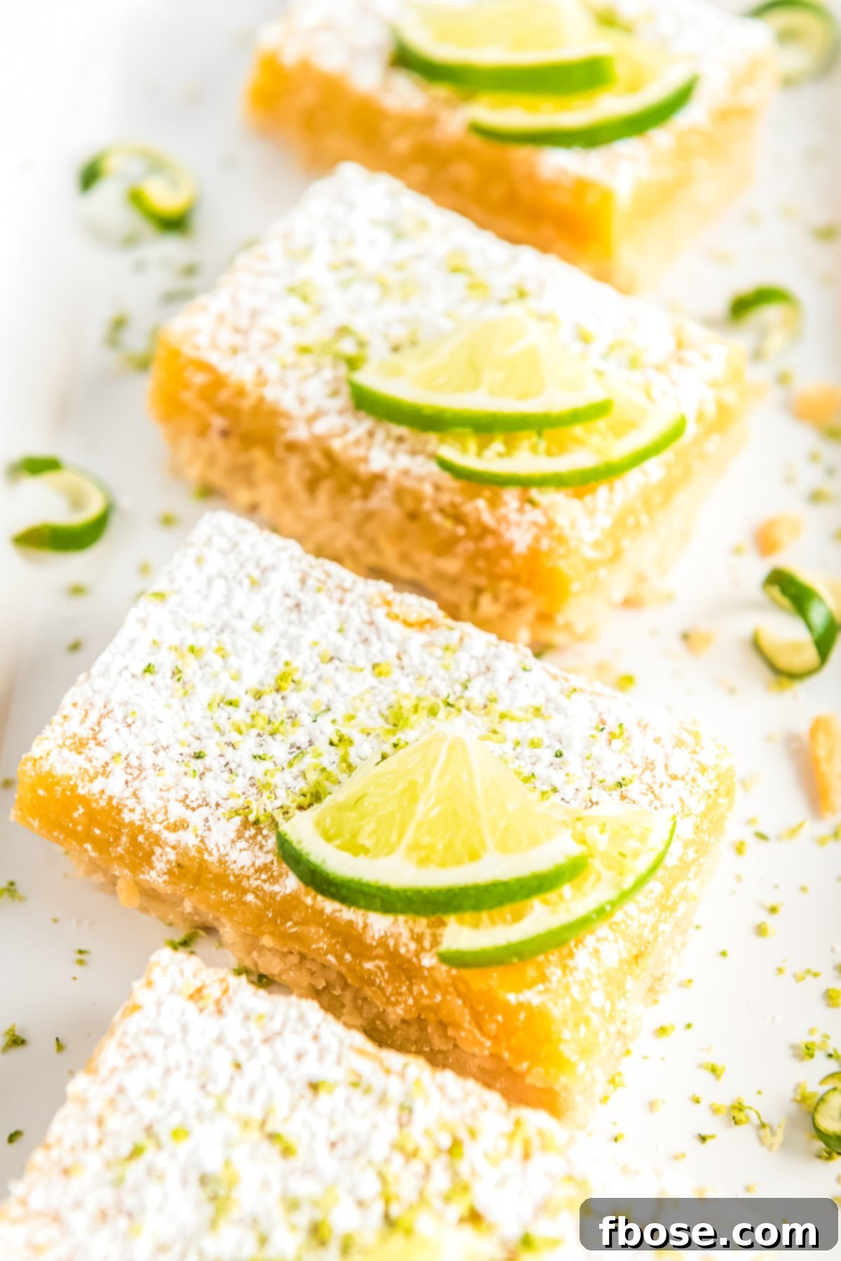 Key Lime Bars arranged on a white plate, garnished with fresh lime wedges and a dusting of powdered sugar.