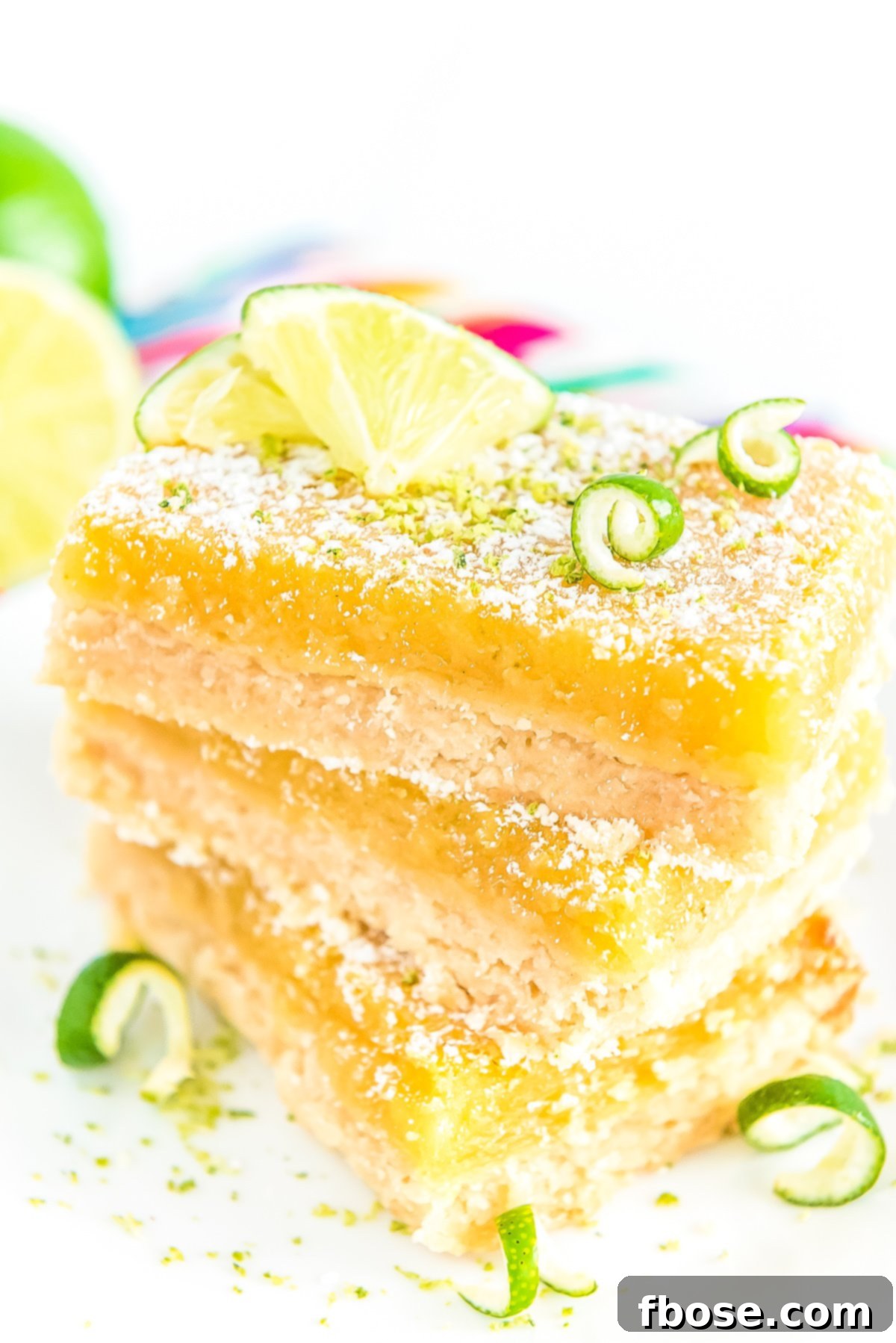 A stack of Key Lime Bars on a white plate, beautifully garnished with a dusting of powdered sugar and delicate lime zest.