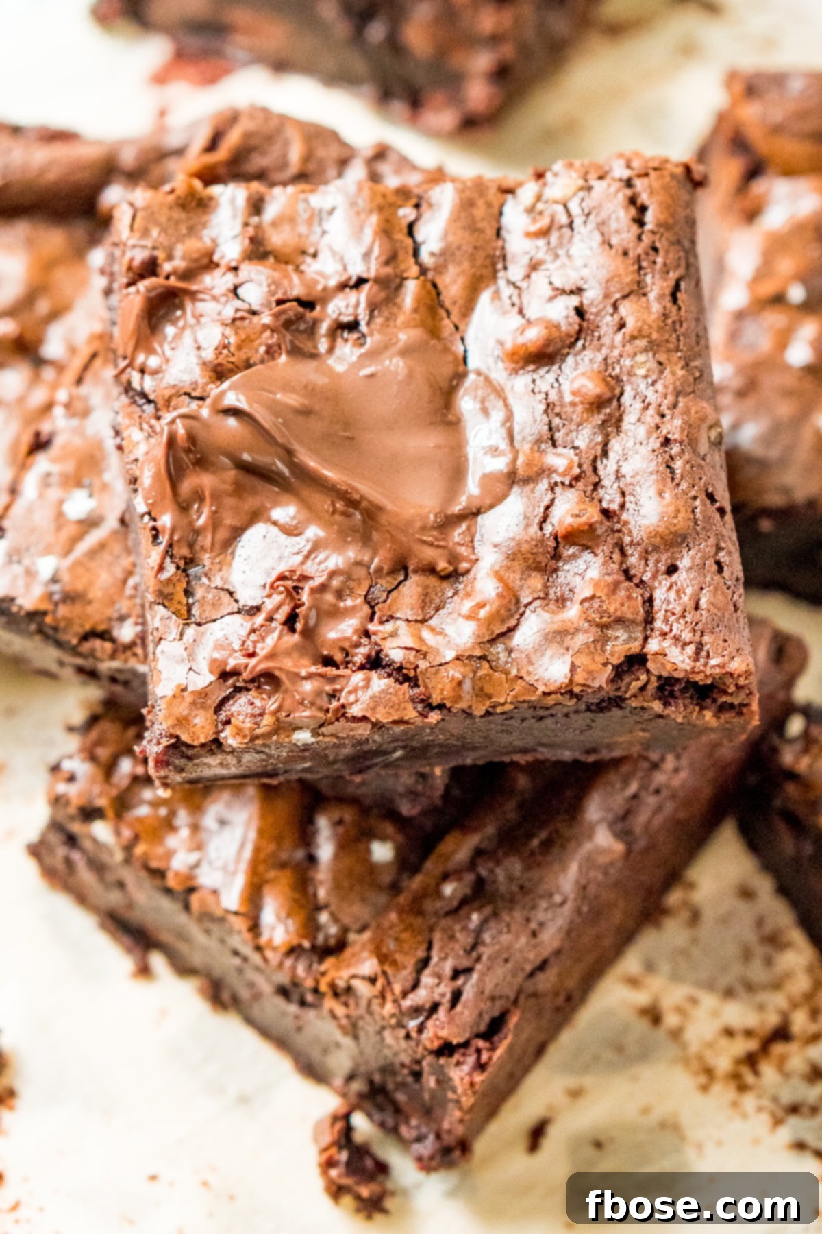 Fudgy Olive Oil Delights 2 Perfectly cut Olive Oil Brownie squares stacked neatly on parchment paper, showcasing their fudgy texture.