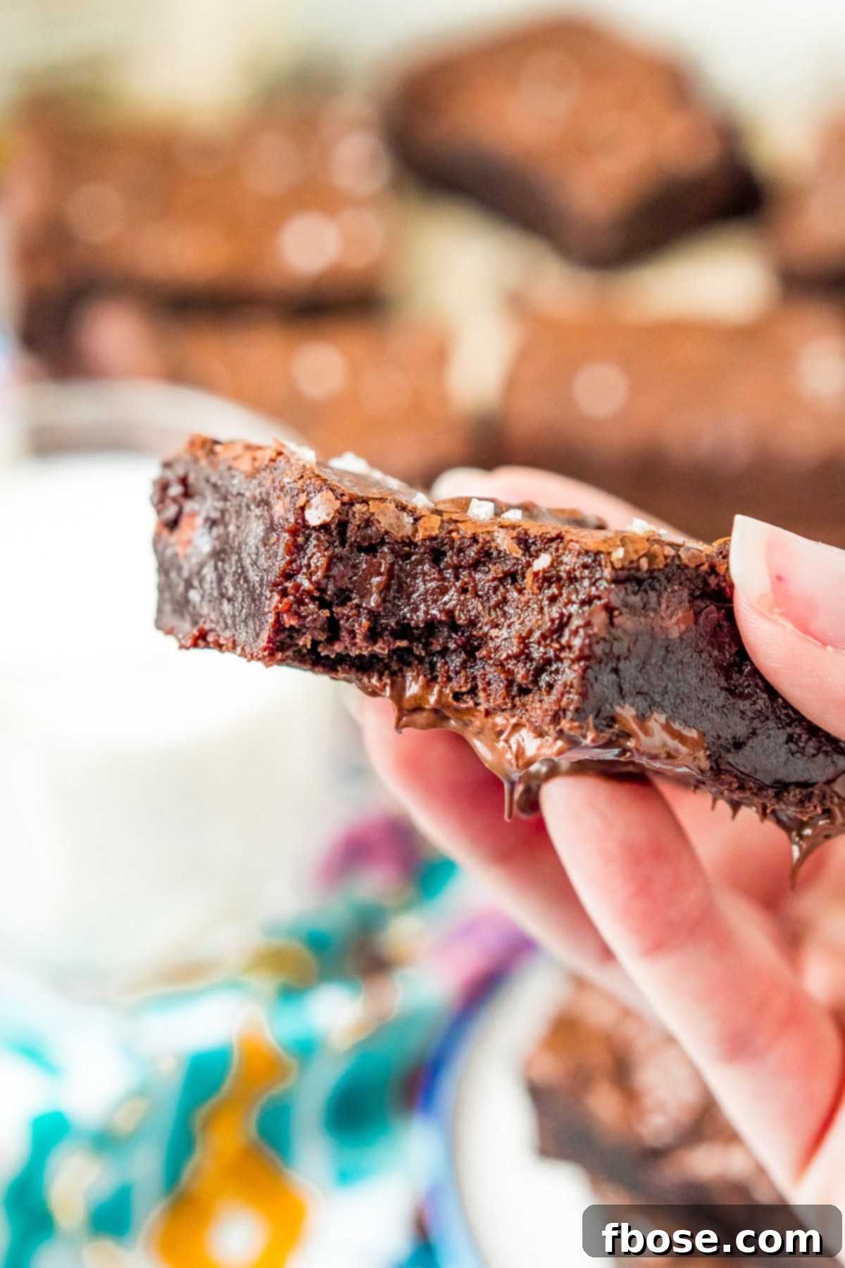 Fudgy Olive Oil Delights 5 A woman's hand holding a bite-taken Olive Oil Brownie, showing its delicious, fudgy interior.