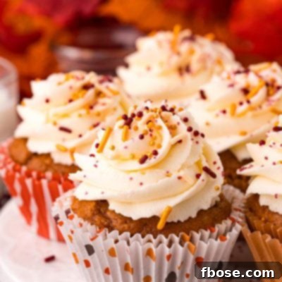 Close up photo of pumpkin cupcakes on a white cake stand with leaves in the background, showcasing the festive autumn theme.