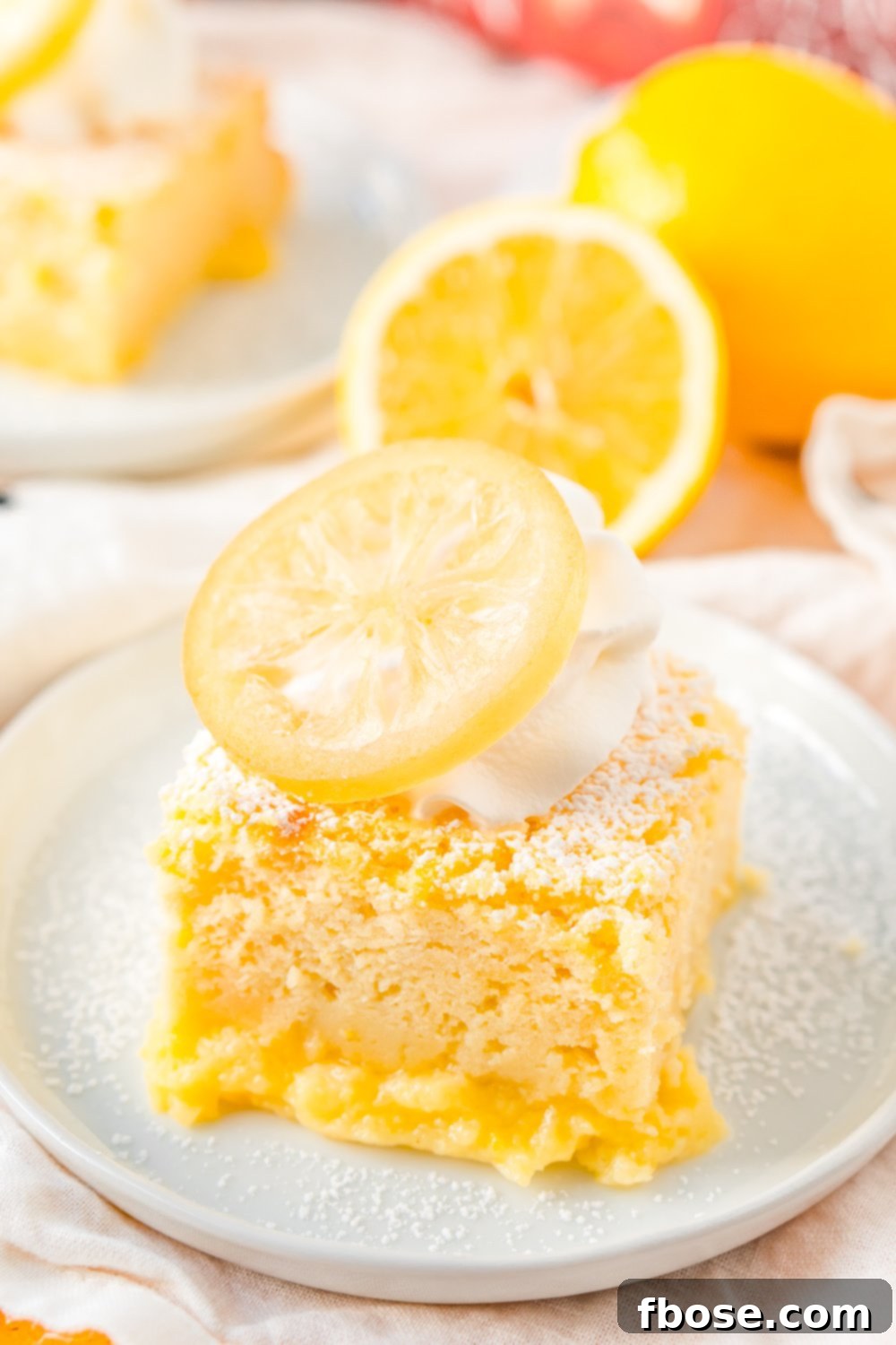 Lemon Cake on small white plate with lemon in the background.