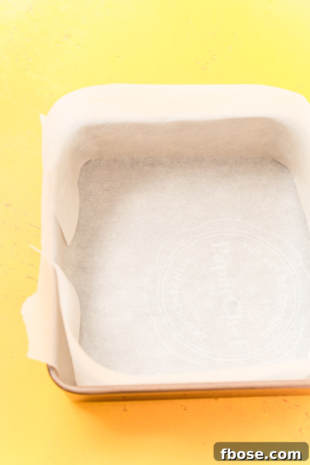 Parchment paper lining a baking pan on yellow surface.
