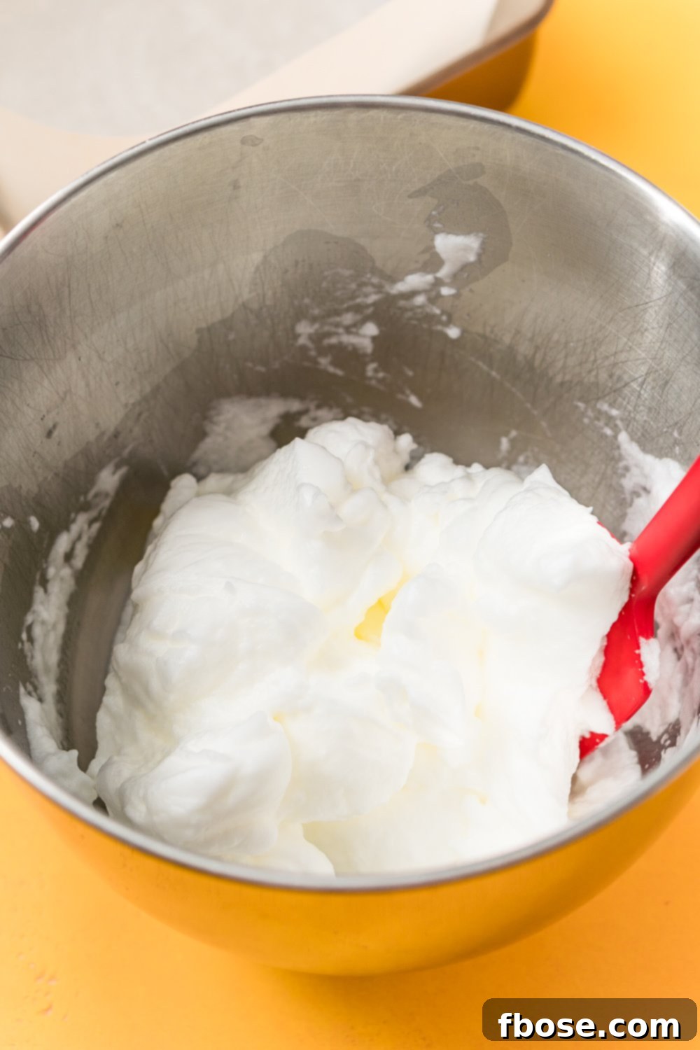 Egg whites that have been beaten stiff in a metal mixing bowl.