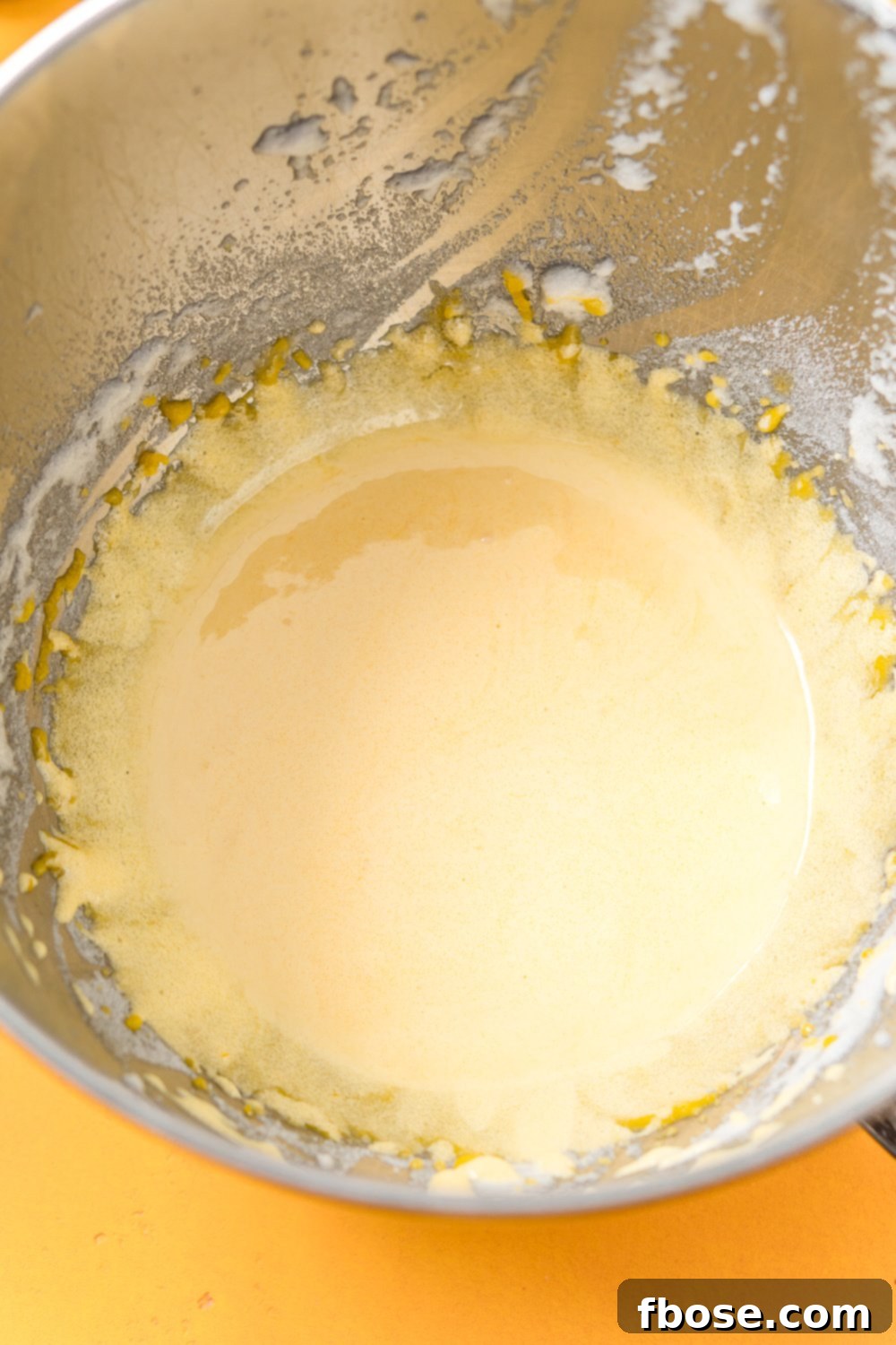 Egg yolks and sugar beaten together in a metal mixing bowl.