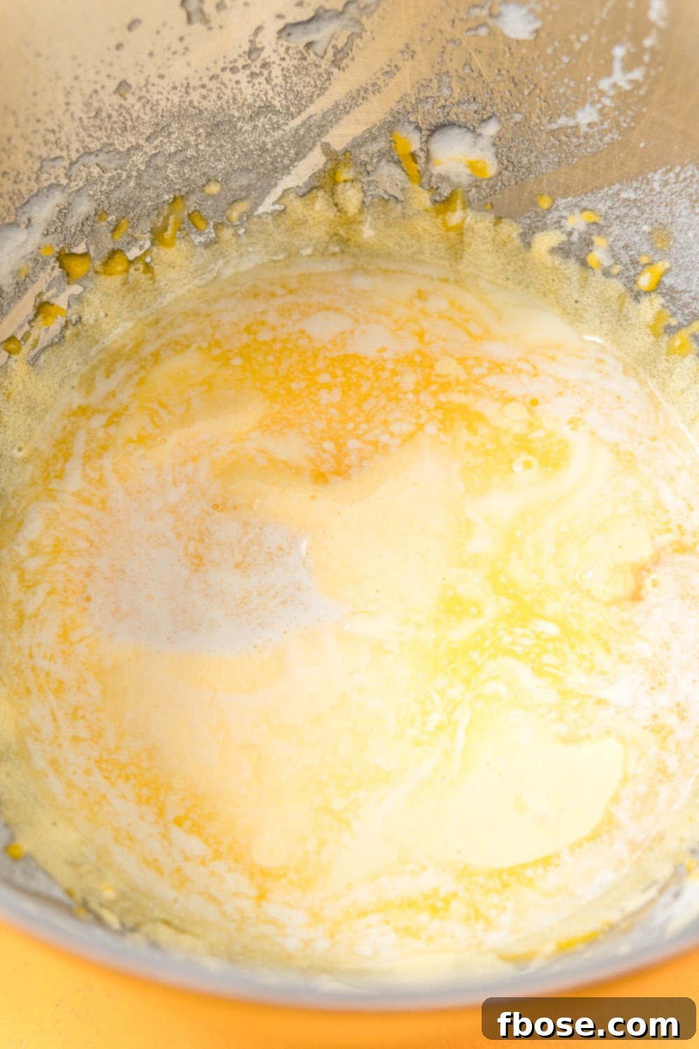 Melted butter being added to lemon cake batter in metal mixing bowl.