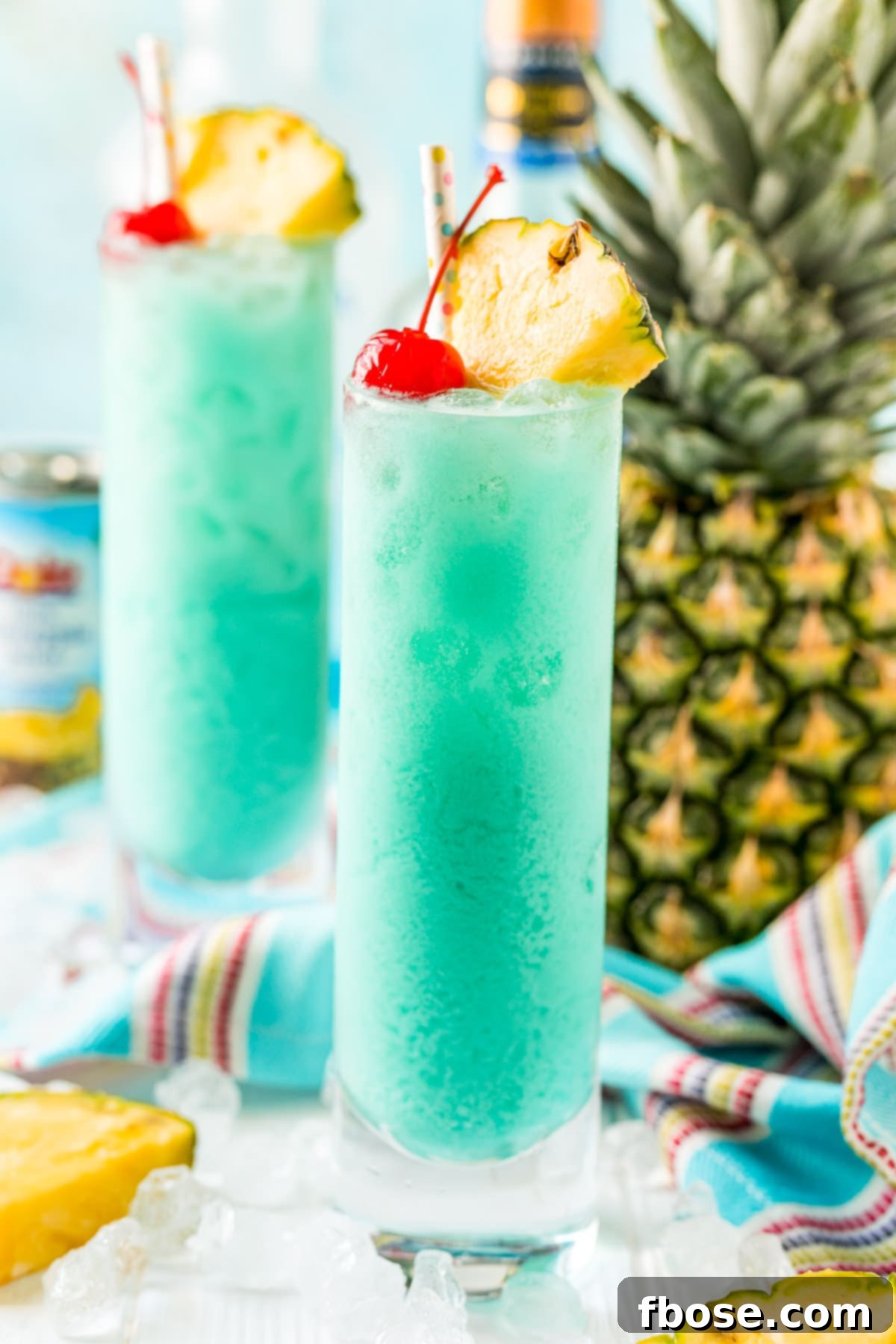 Azure Aloha 2 Close up photos of two classes filled with a blue cocktail with a pineapple in the background.