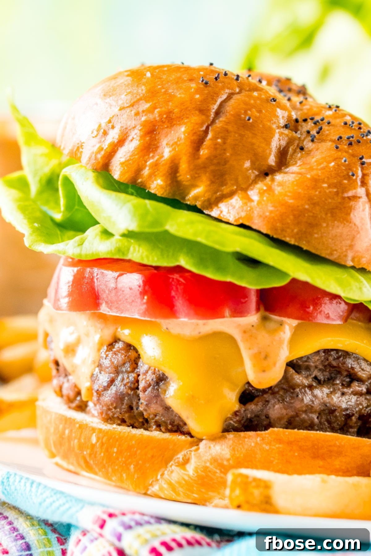 Close up photo of a juice burger topped with cheese, sauce, tomato, and lettuce.