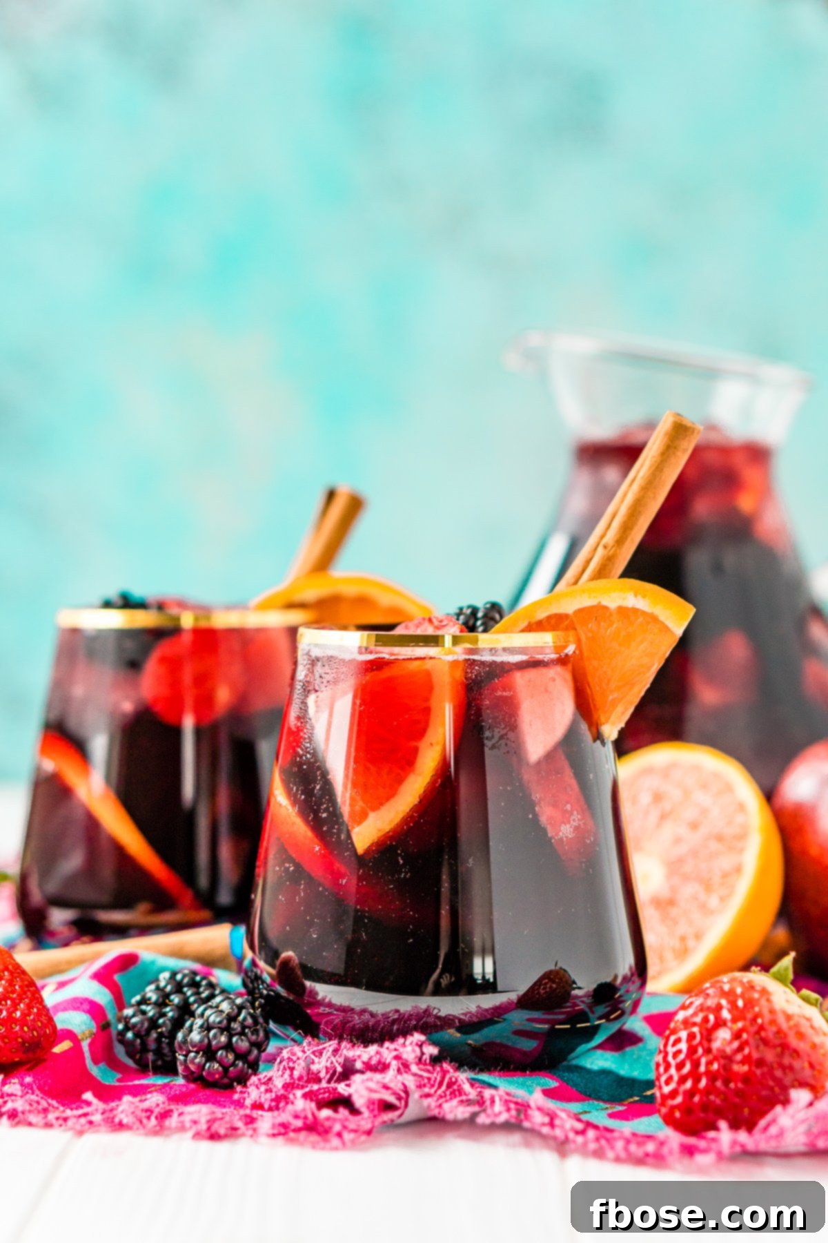 Multiple glasses of ruby-red wine sangria sit invitingly in front of a generously filled pitcher, surrounded by an artful scattering of fresh, colorful fruits.