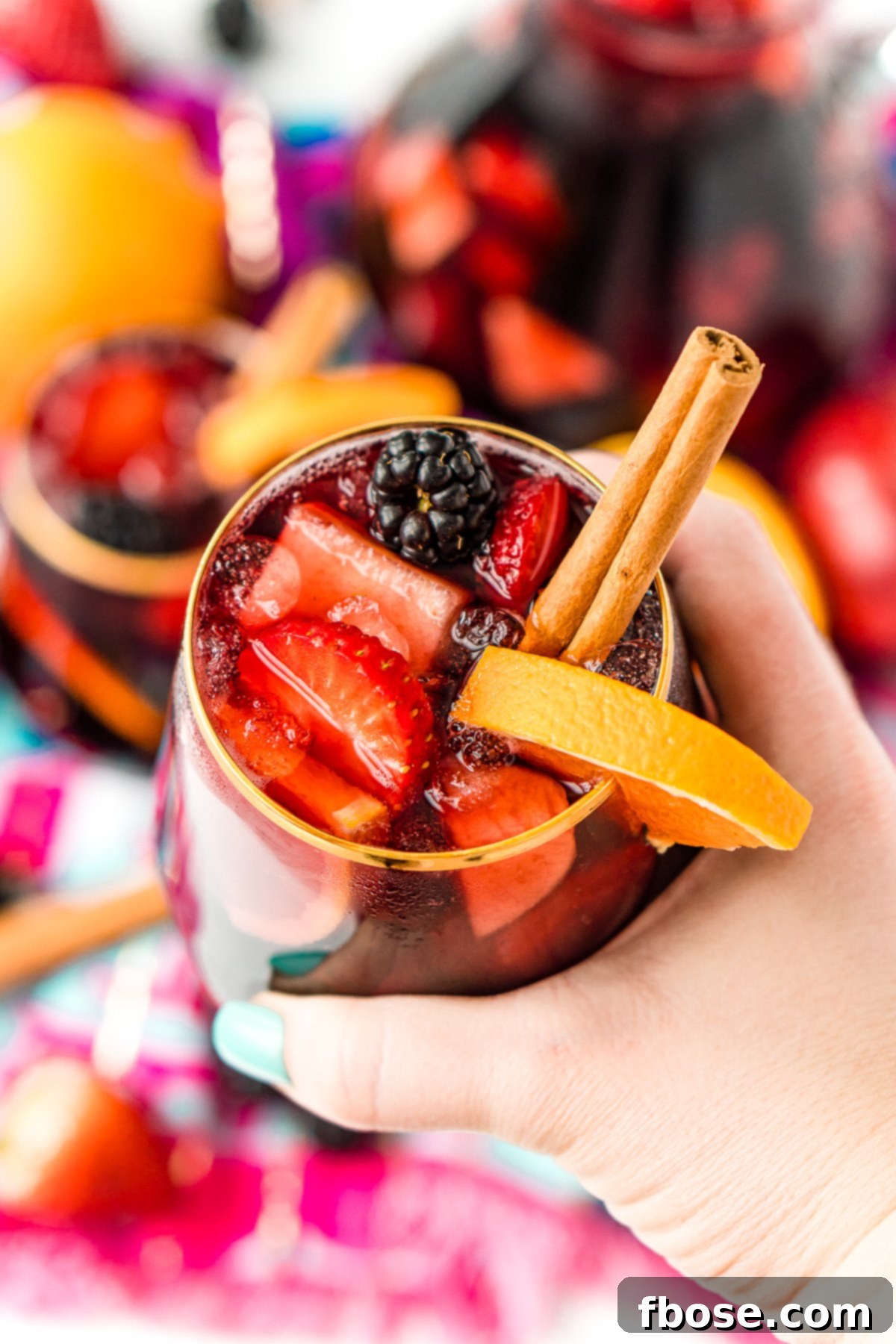 A woman's hand gently holds a glass filled with vibrant red sangria, captured in a warm and inviting light.