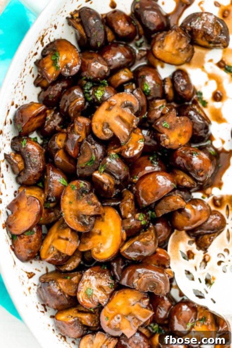 Overhead photo of perfectly browned sauteed mushrooms with balsamic glaze in a white skillet, garnished with fresh herbs.