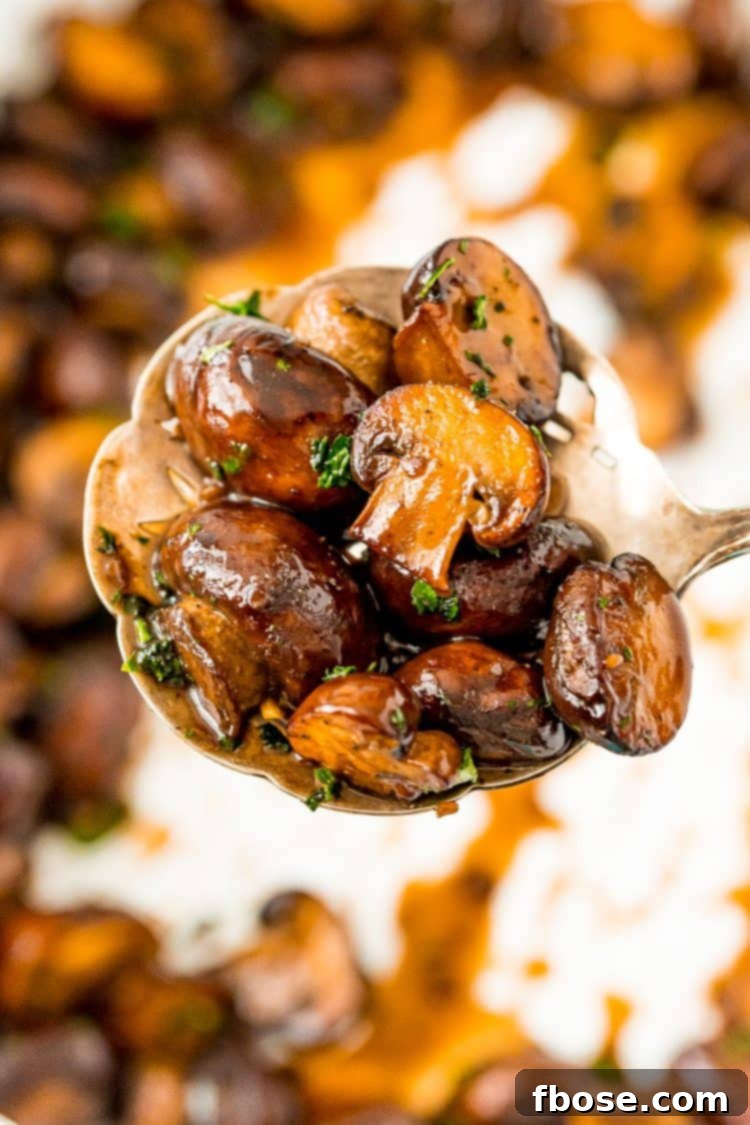 Serving spoon lifting a portion of glistening, browned sauteed mushrooms from a white skillet.