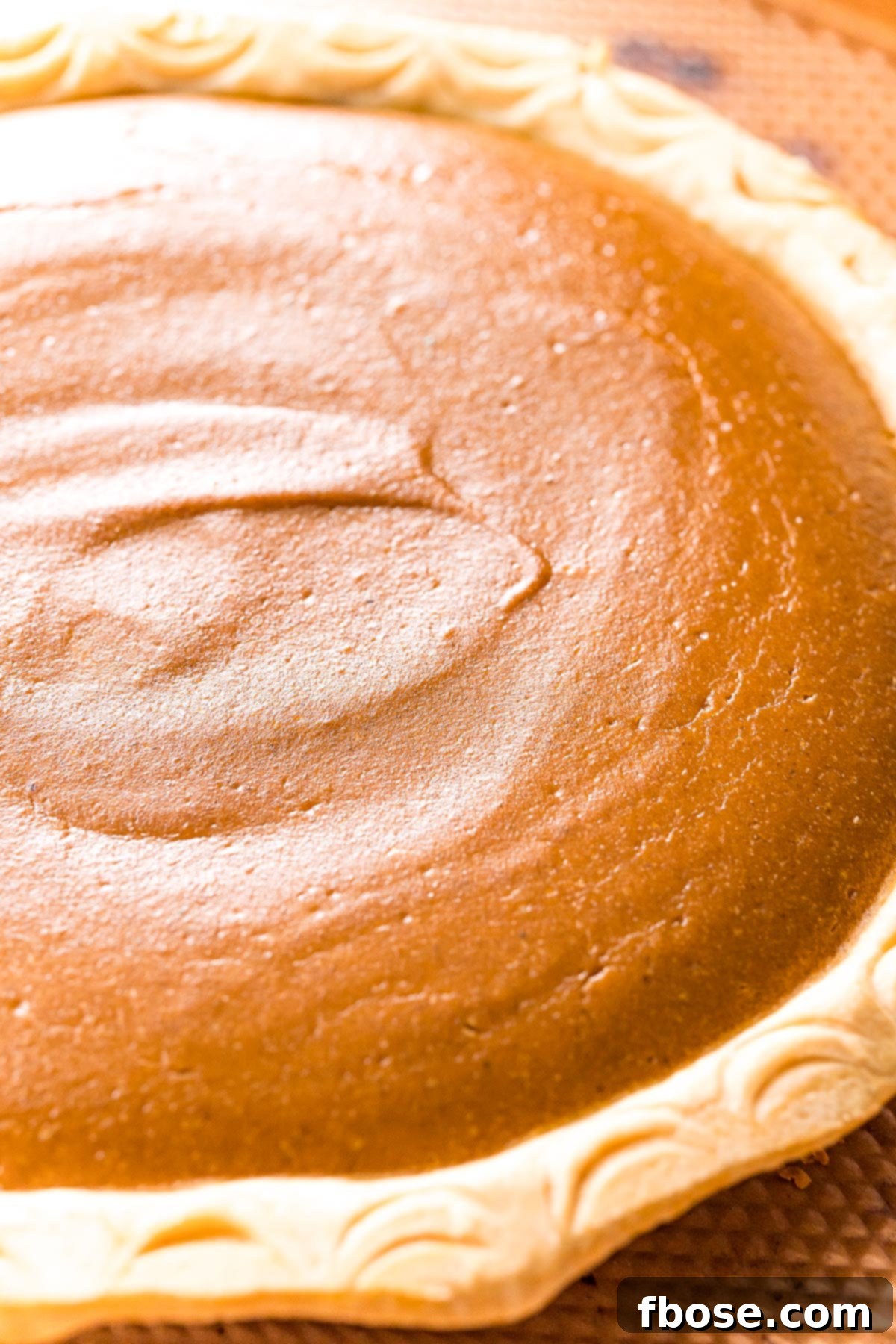The Ultimate Pumpkin Pie 5 A close-up view of a perfectly baked pumpkin pie, showcasing its smooth, set filling and golden-brown crust, indicating ideal doneness.
