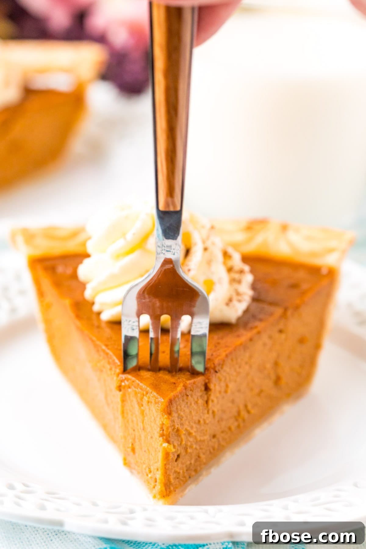 The Ultimate Pumpkin Pie 6 A fork piercing into a delicious slice of pumpkin pie, showcasing its creamy texture and flaky crust.