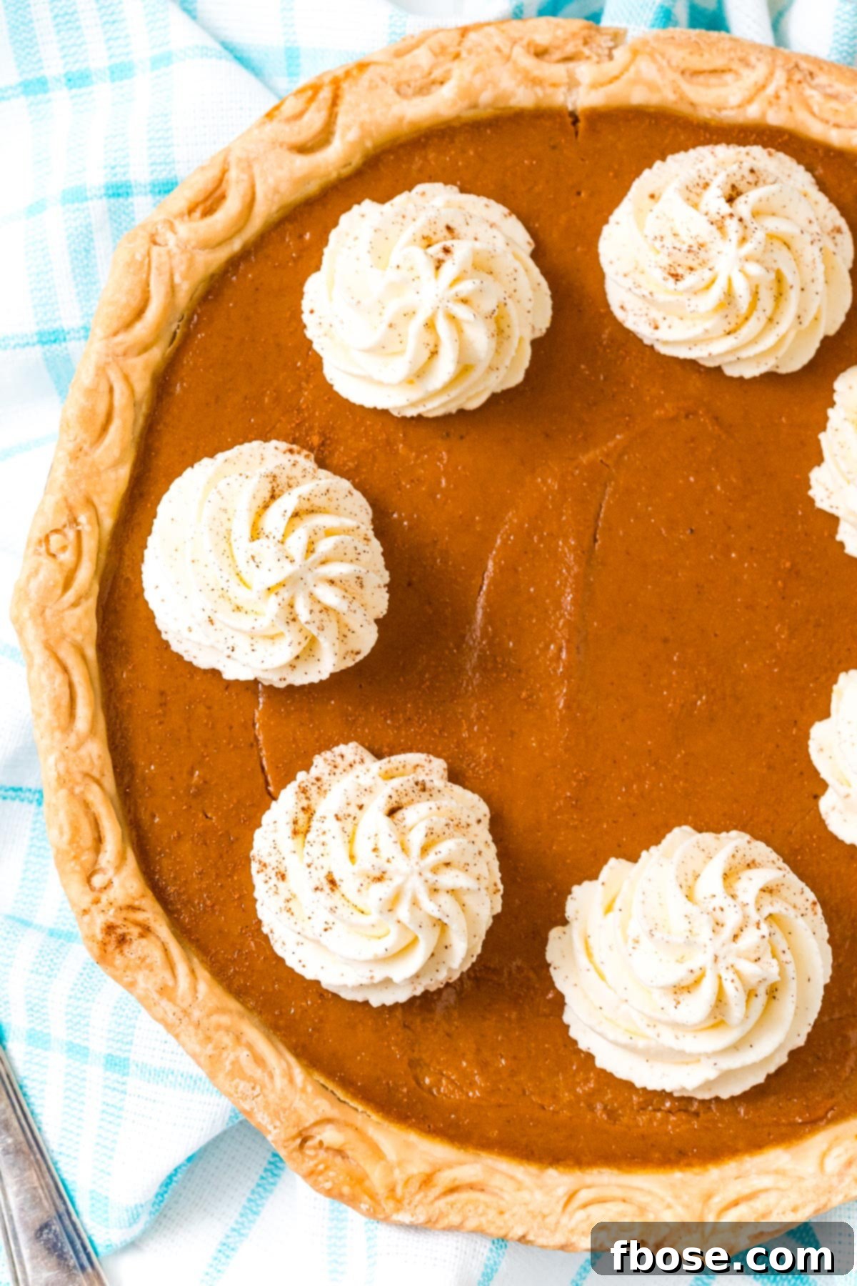 The Ultimate Pumpkin Pie 8 An overhead shot of a freshly baked pumpkin pie, elegantly topped with dollops of fluffy whipped cream, invitingly ready for serving.