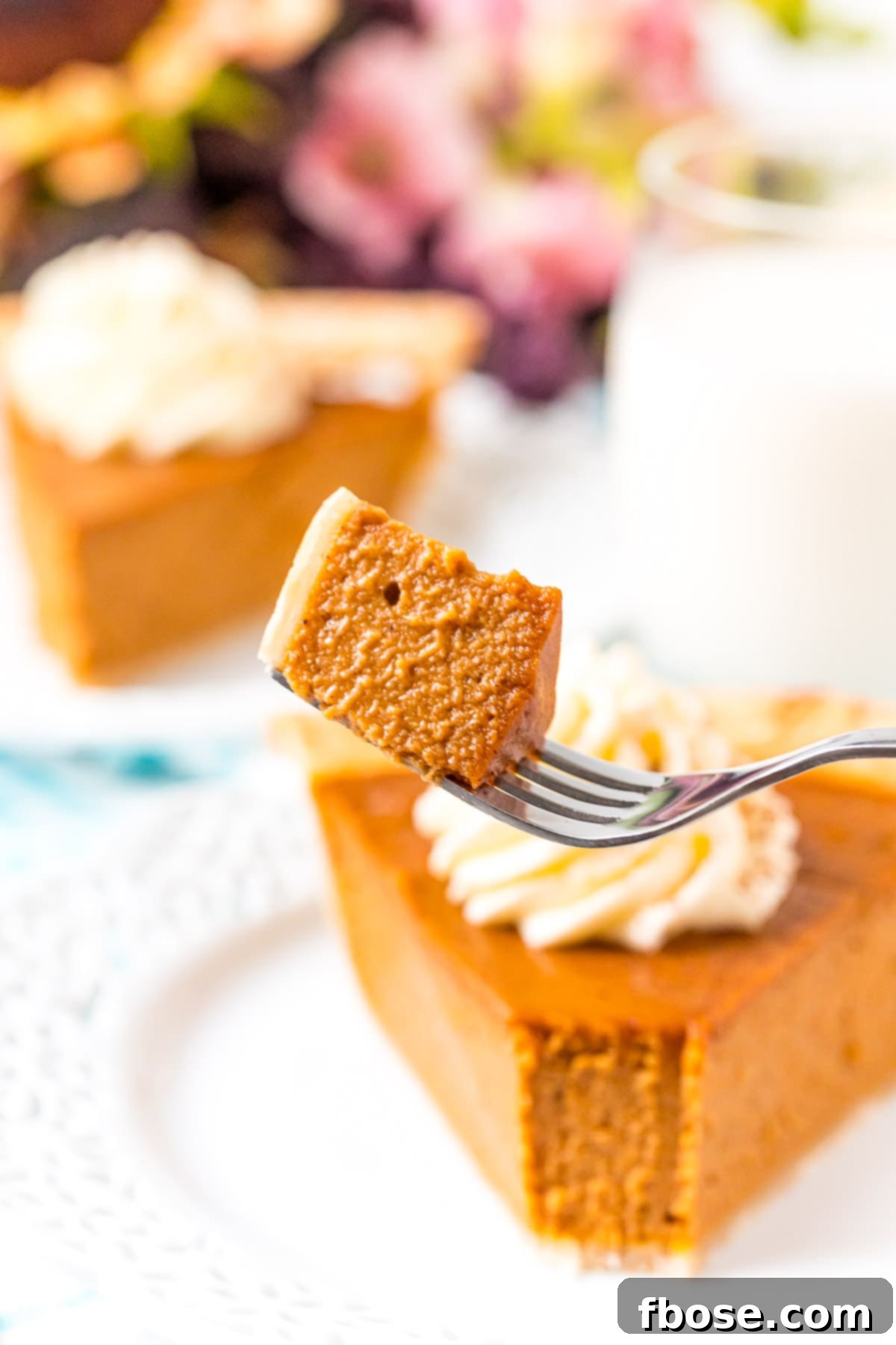 The Ultimate Pumpkin Pie 9 A close-up of a fork holding a perfect bite of pumpkin pie, with more slices visible in the blurred background, highlighting the pie's tempting texture.