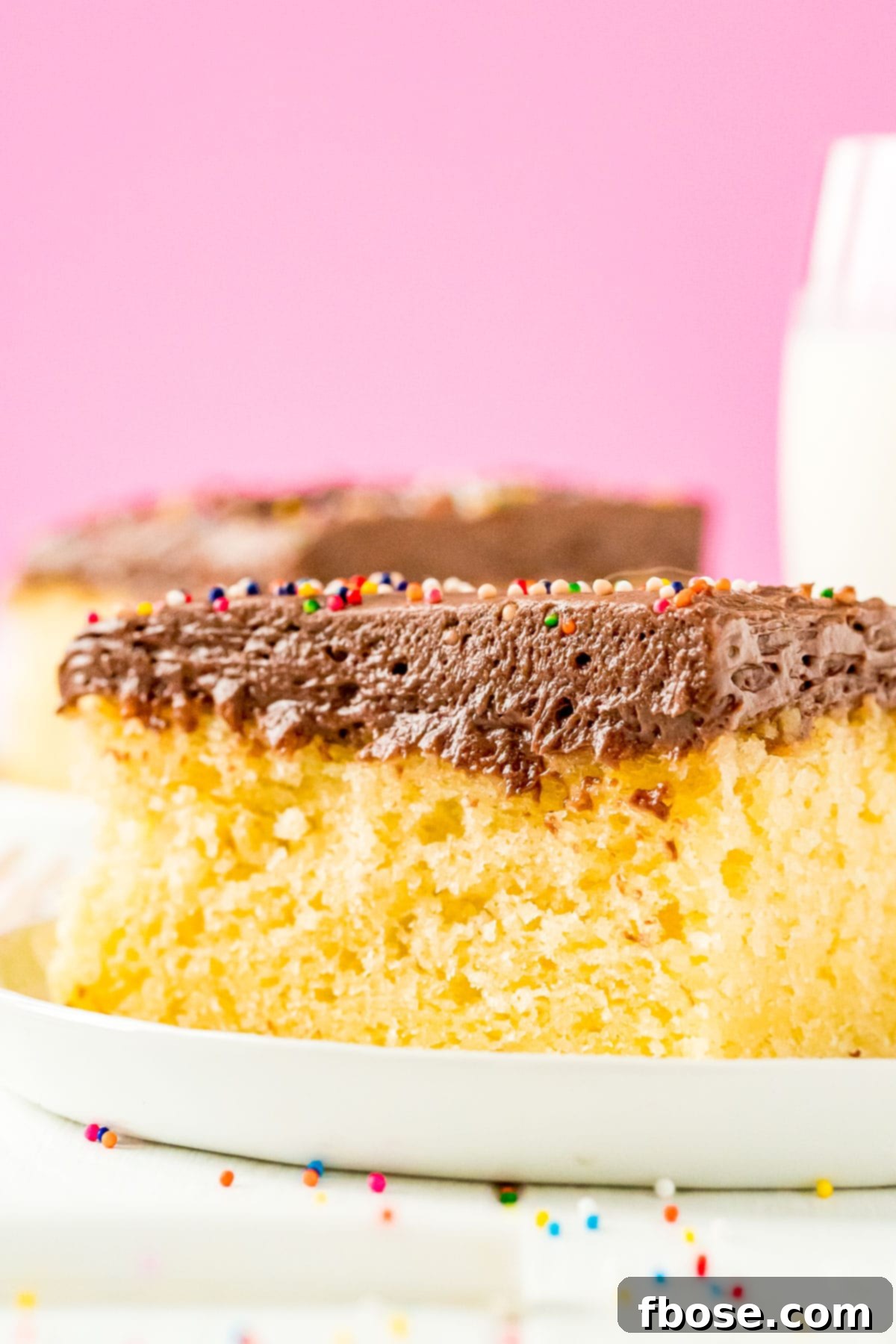 Slice of yellow sheet cake with chocolate frosting on a white plate.