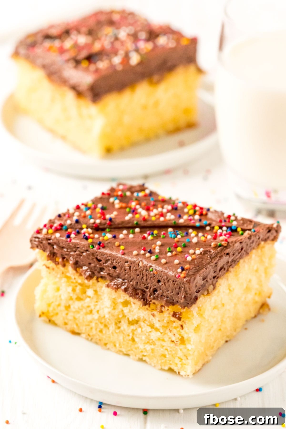 Slices of yellow cake on small white plates with a glass of milk.