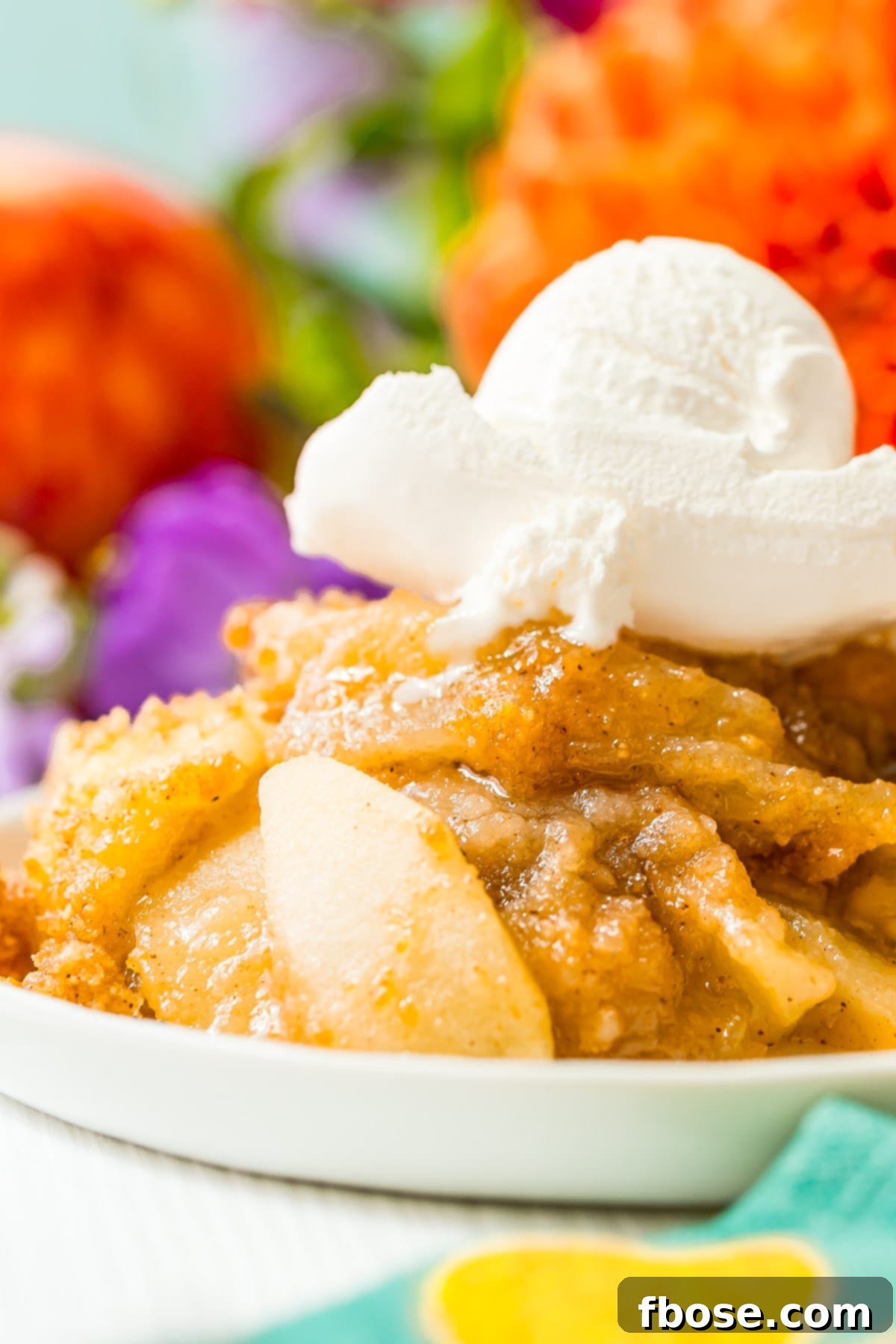 Close up photo of apple brown betty on a white plate topped with ice cream, showcasing its golden crust and soft apple filling.