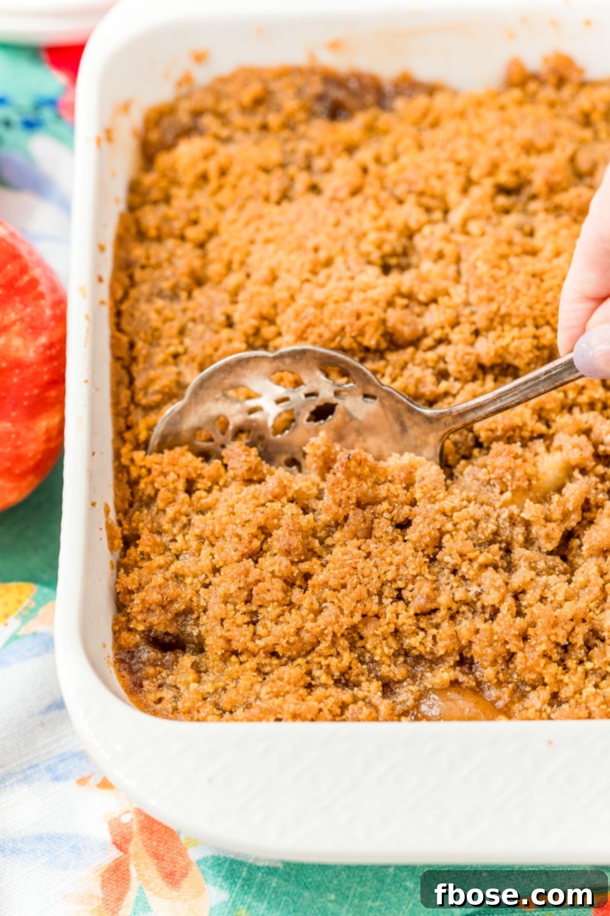 Woman's hand scooping a generous portion of warm apple brown betty out of a rustic baking dish, highlighting its comforting appeal.