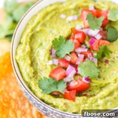Guacamole 8 Close up photo of a bowl of guacamole garnished with diced tomatoes, cilantro, and red onion.
