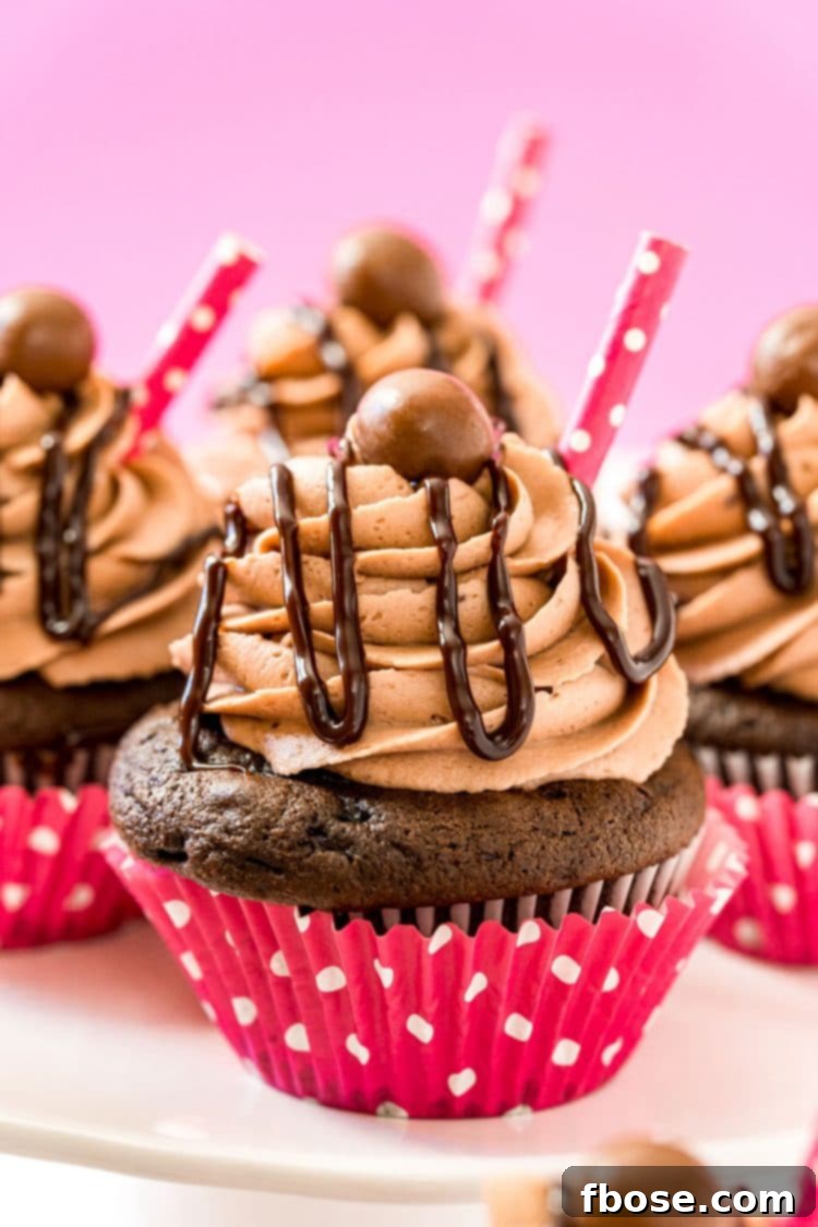Decadent chocolate cupcakes in festive pink wrappers, lavishly topped with rich chocolate malt frosting and a delicate chocolate sauce drizzle.